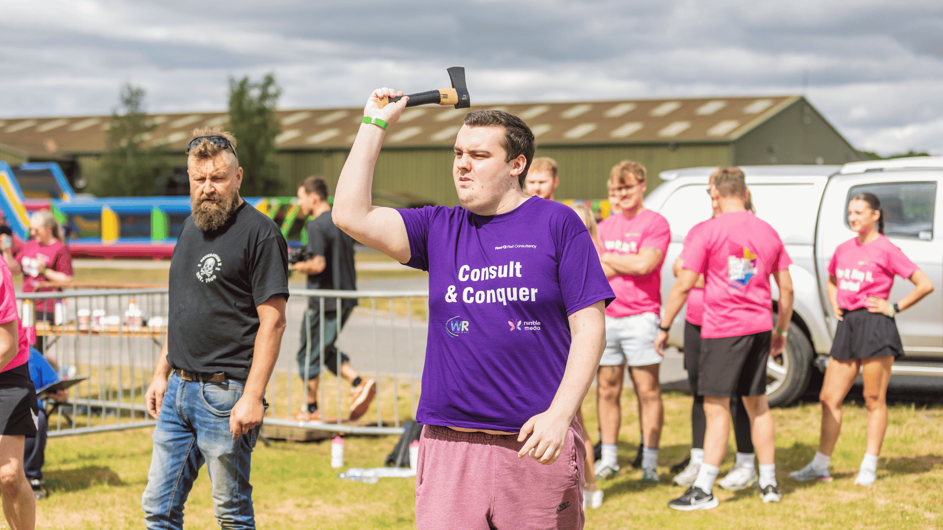 Outdoor team-building event with participants wearing matching blue shirts, taking part in inflatable obstacle courses and games, smiling and cheering, with the words 'ENTER A TEAM' in large bold white and green text across the image.