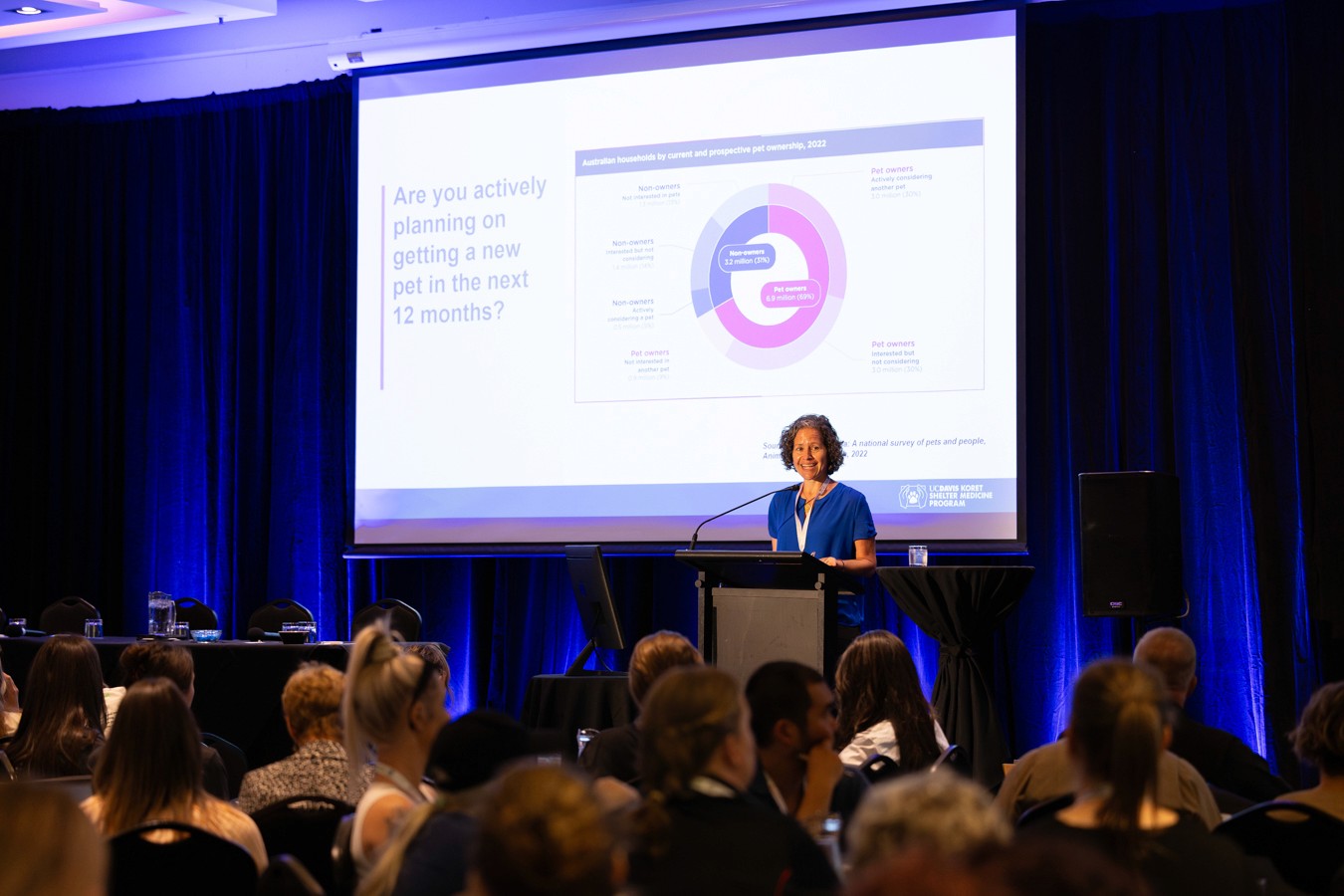 Woman speaking on stage at conference next to projector screen