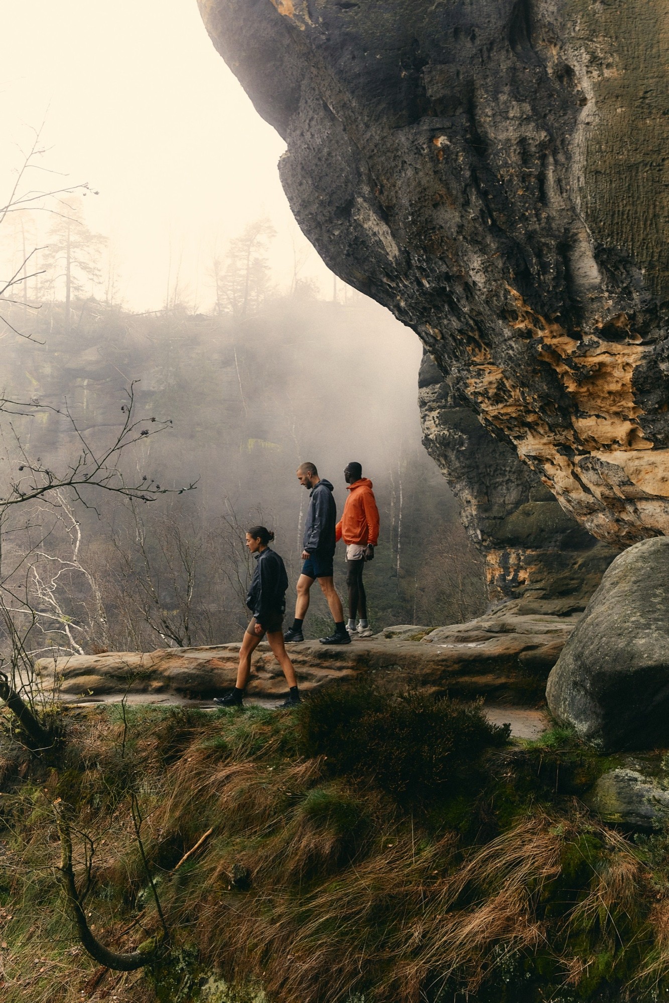 Three figures on a ledge beneath a rock overhang in fog