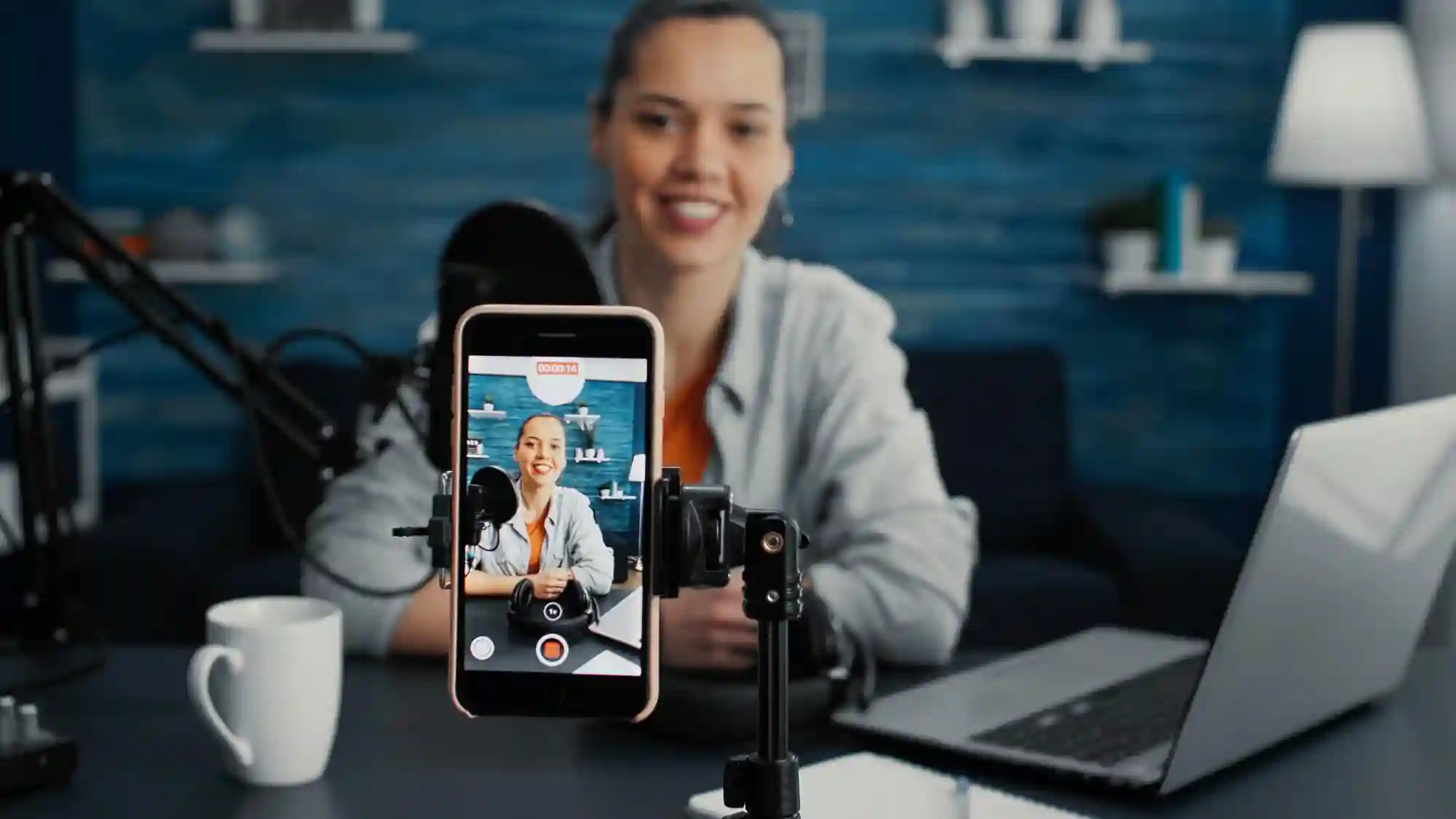 Vlogger recording a podcast or live video on a smartphone mounted on a tripod with a microphone setup.