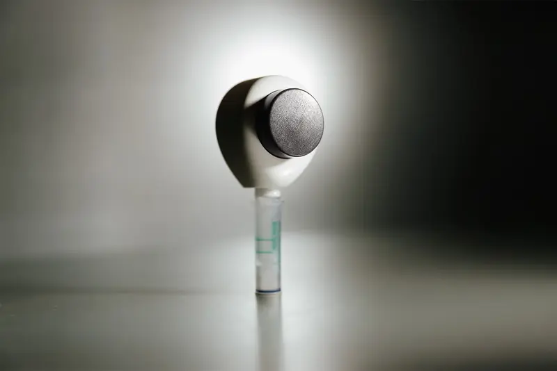 Rythm Health at-home testing device with a sample tube attached, shown against a clean, minimal background.