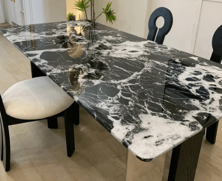 A rectangular dining table with a glossy black marble top featuring striking white veining. The table is paired with modern, minimalist chairs in a stylish dining room setting.