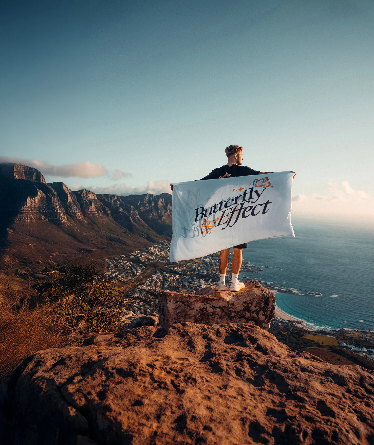 Lee Hutchinson holding a butterfly effect flag on the top of a mountain