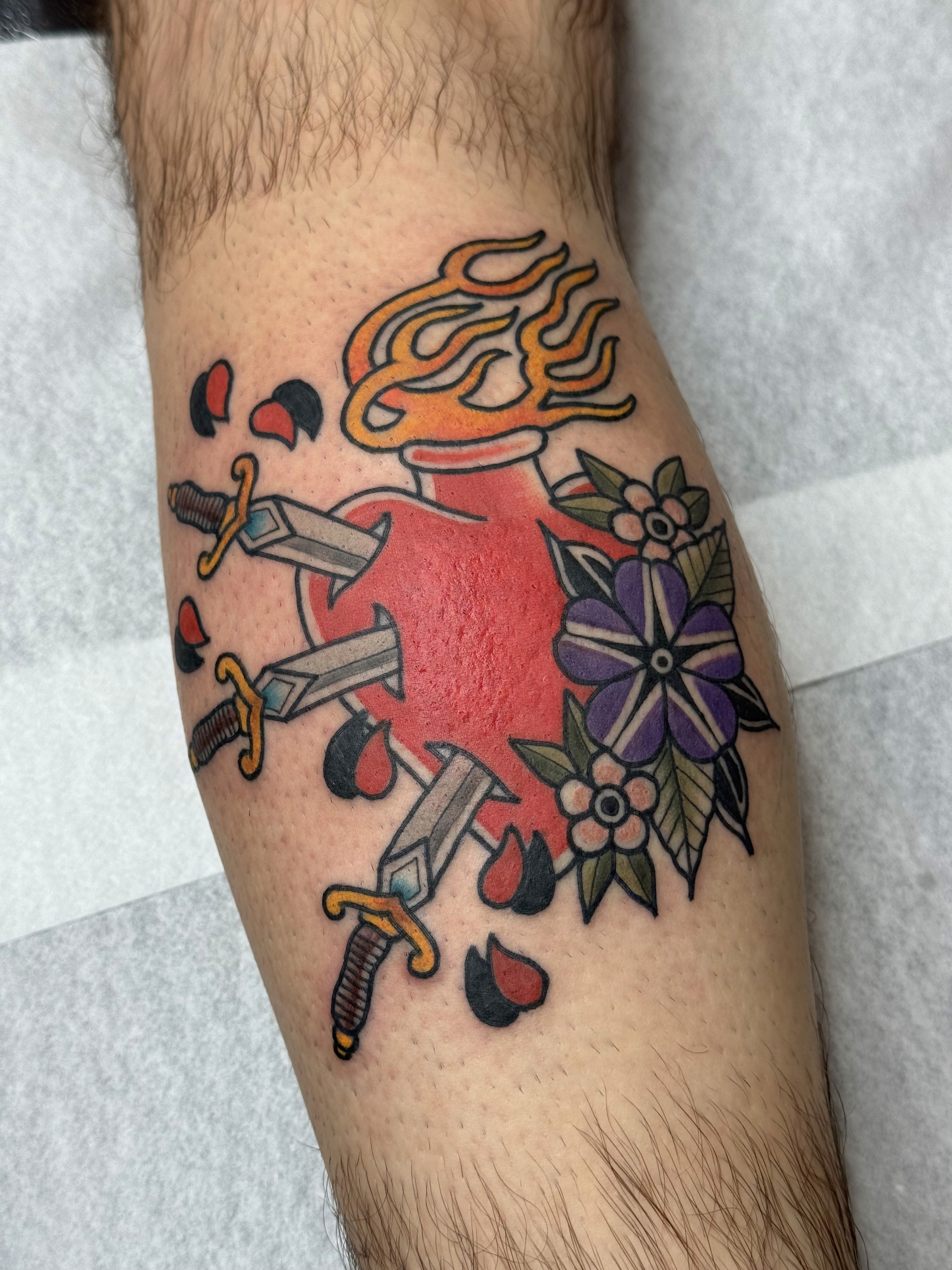American traditional flaming heart tattoo pierced by three daggers with purple and pink flowers, tattooed by Andy at Whambam Tattoo at Bristol Tattoo Convention