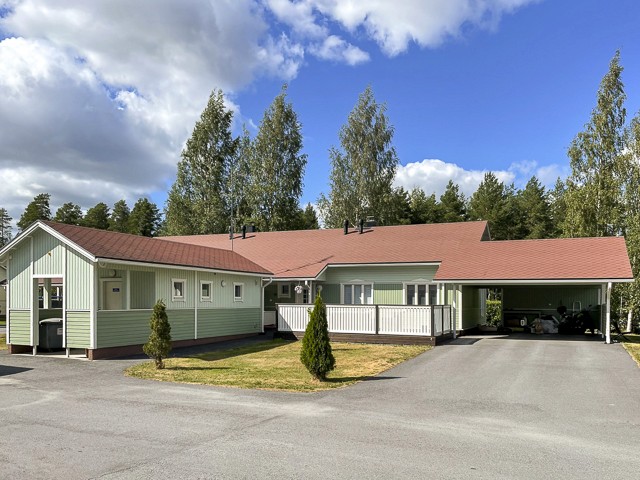 Ulkomaalattu paritalo Seinäjoella, mintunvihreä julkisivu punaisella tiilikatolla, katos autolle, avara piha-alue ja metsäinen tausta.