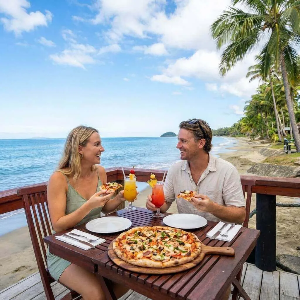 Smiling couple enjoys pizza and cocktails on a beachfront deck at Uprising Beach Resort, Fiji.