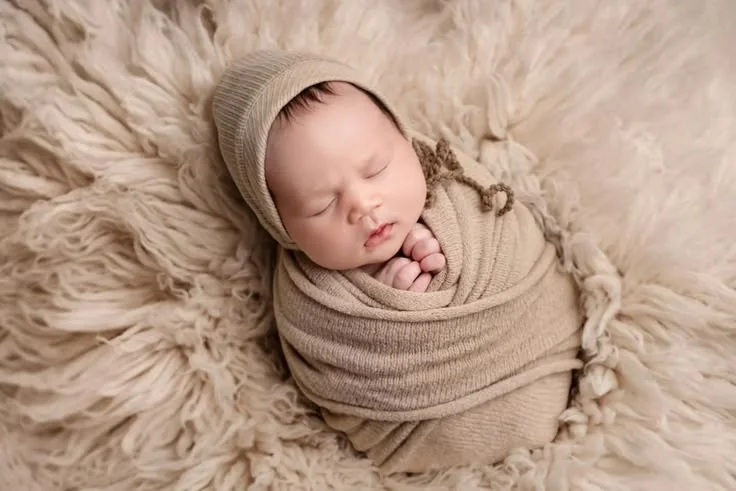 Newborn wrapped in beige fabric on a fluffy cushion