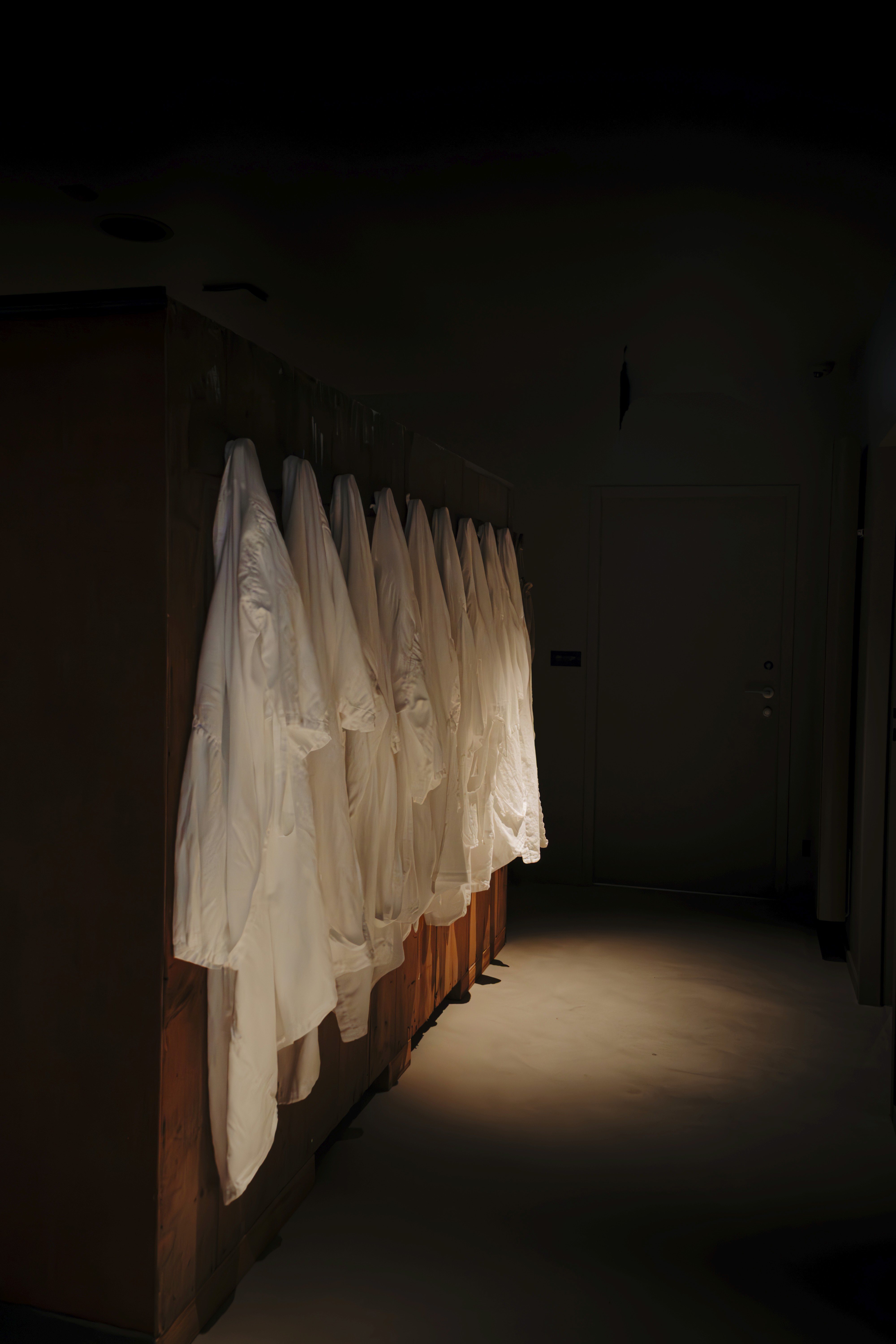 Young woman with short, dark hair and a yellow sweater looks serious, surrounded by hands holding smartphones, conveying intrusion and tension.