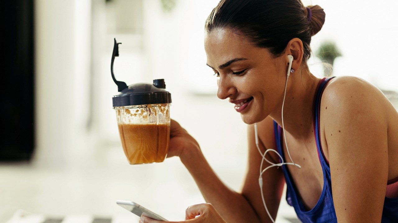 woman drinking protein shake while using a smartphone