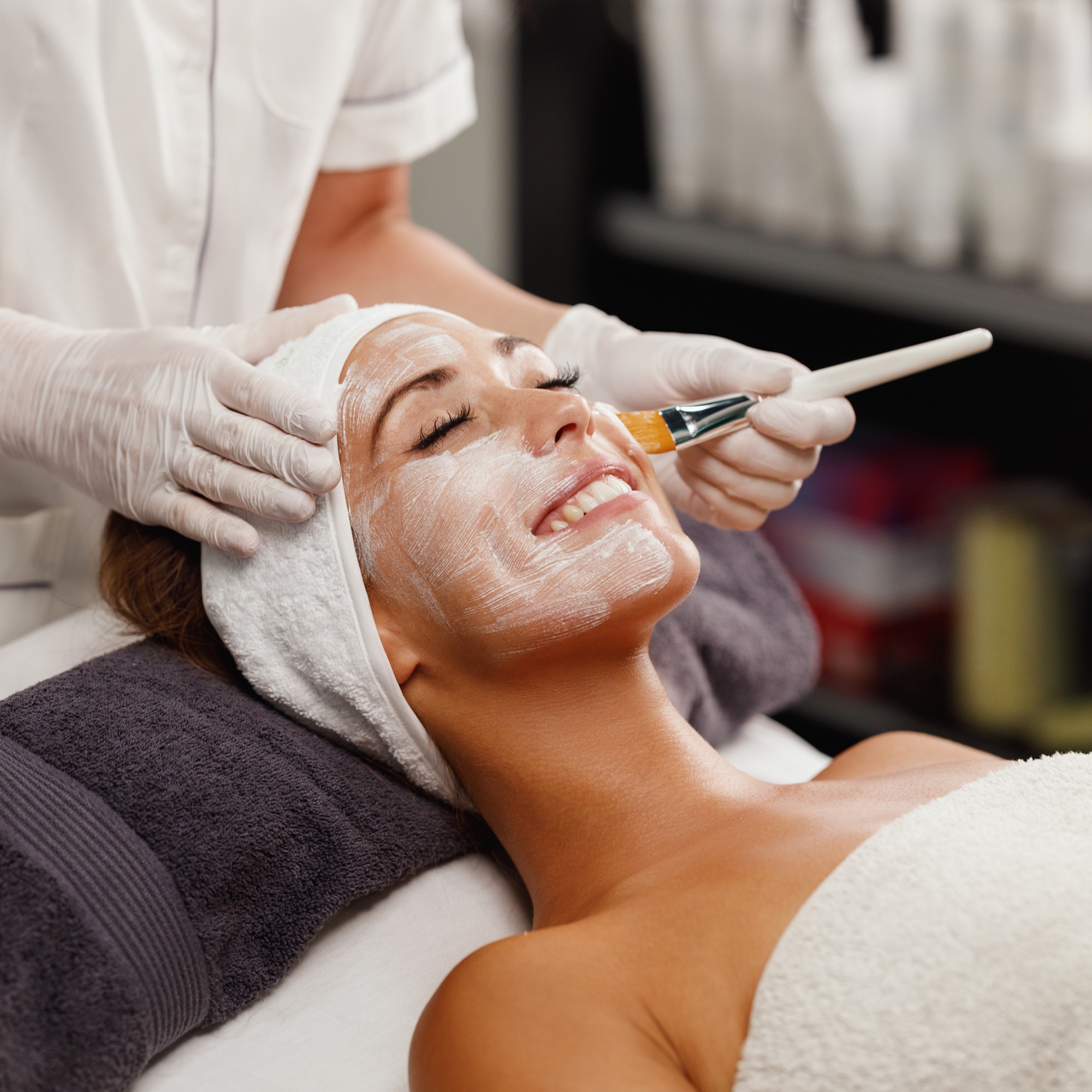 Close-up of a woman with under-eye gel patches, natural makeup, and smooth skin, against a neutral beige background