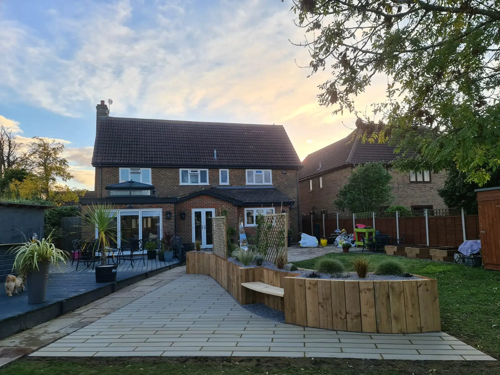 A cozy house with a patio and outdoor seating, surrounded by greenery during sunset.