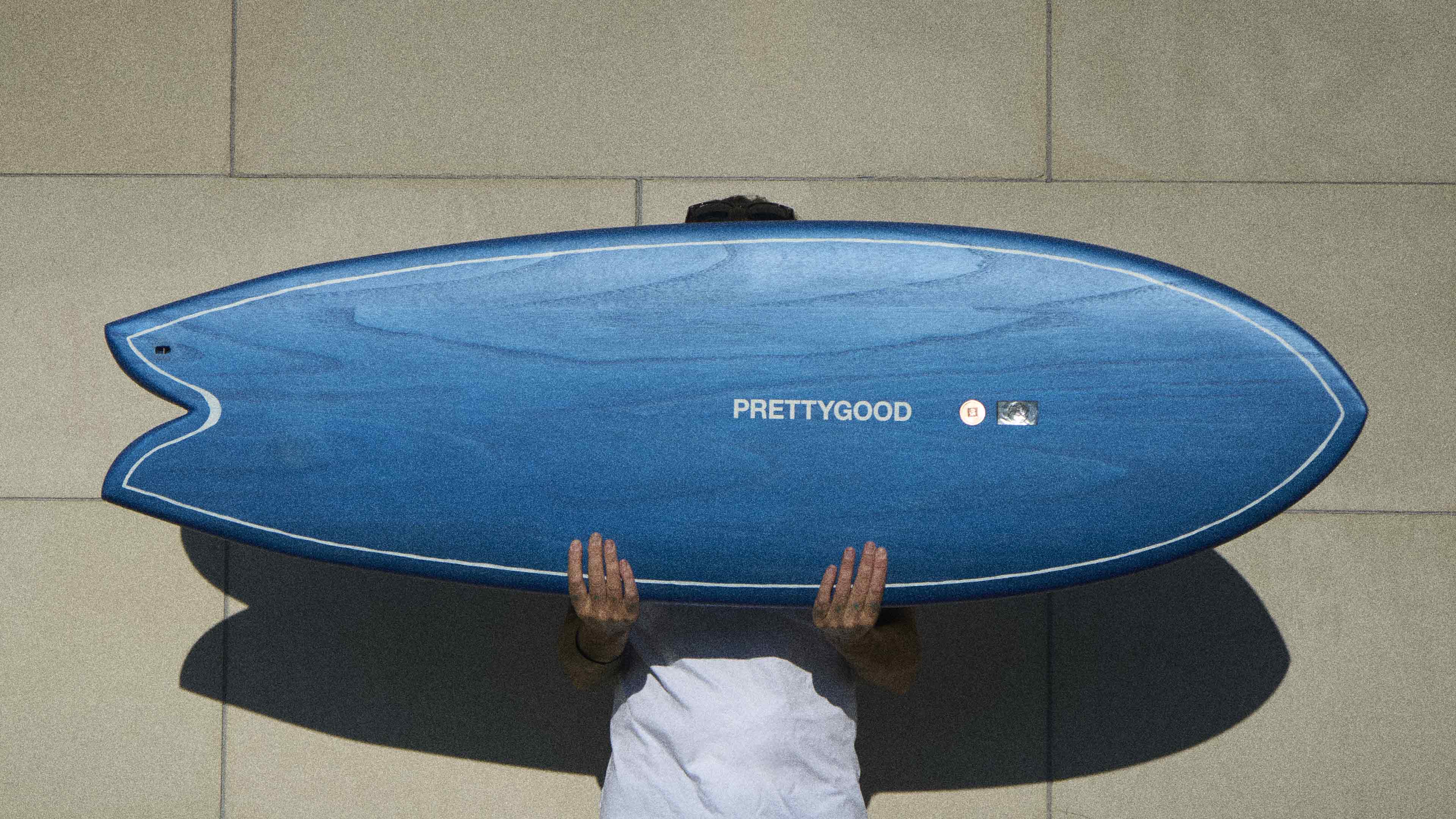 Surfboard shaper holding a blue twin fin fish