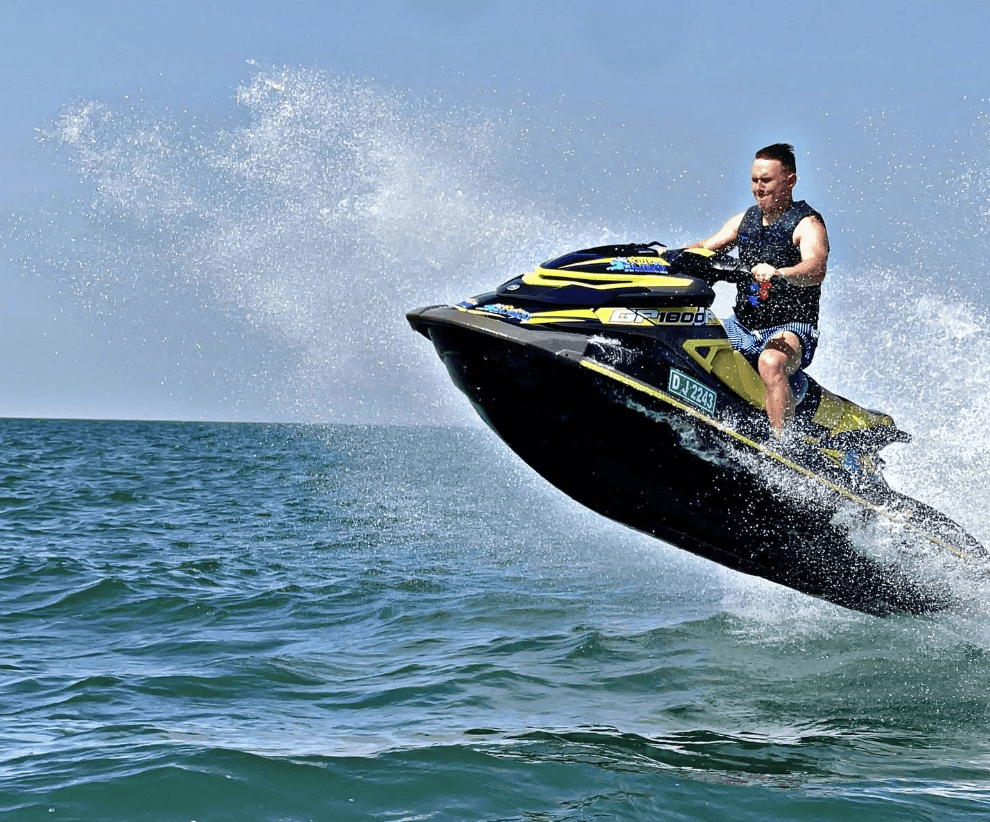 A man manoeuvring a high-speed jet-ski across the open sea, with the front of the vessel lifted into the air