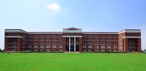University Picture from front. It is a huge building with 5 floors and longer than it is wider. It is made of red bricks with white accents. It also has a huge green ground in front of it.