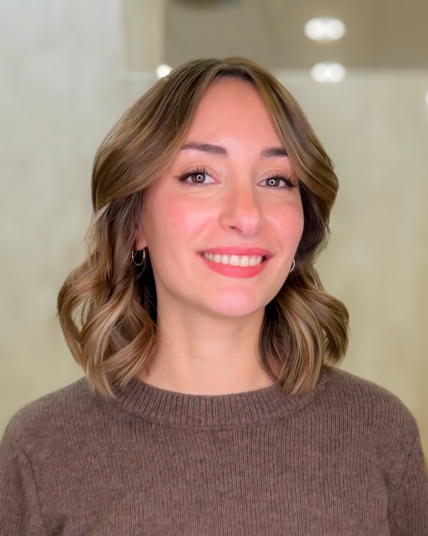 A woman lying on a massage bed, illuminated by soft sunlight streaming through a nearby window. A lush green plant in the background enhances the peaceful and rejuvenating ambiance.