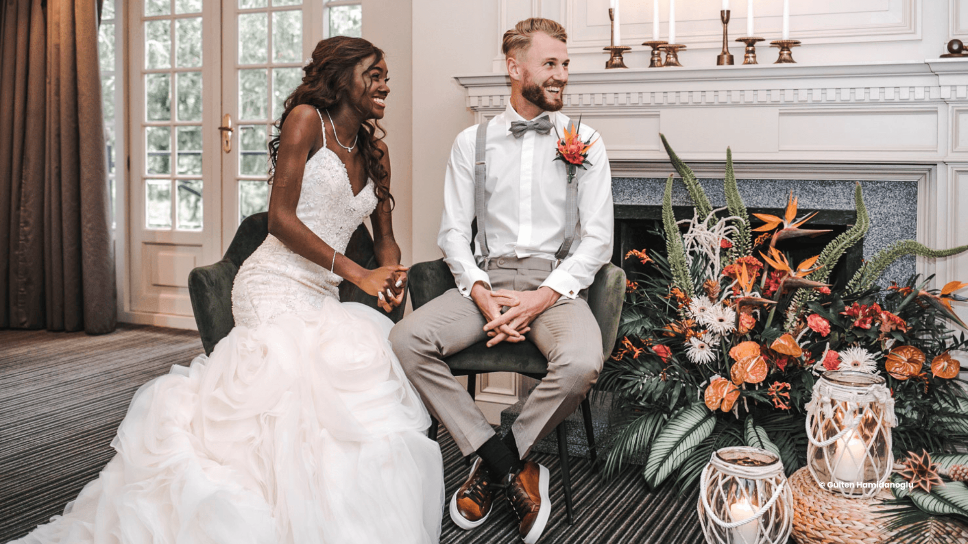 Een stralend bruidspaar zit hand in hand tijdens hun huwelijksceremonie, omringd door bloemen en sfeervolle decoratie — een liefdevolle trouwdag vol trouwinspiratie.