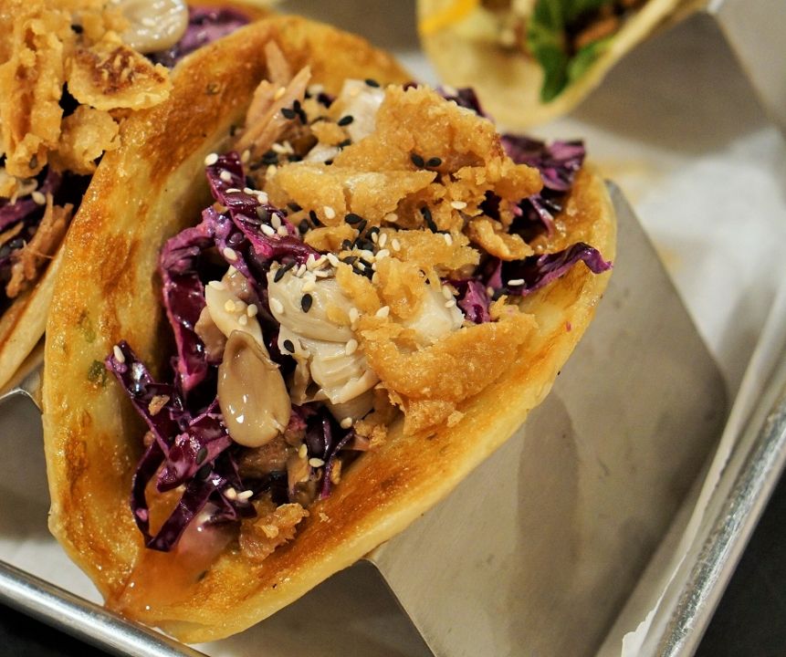 Duck taco on a scallion pancake with confit duck, ginger-cabbage slaw, pickled oyster mushrooms, plum sauce, sesame seeds, and crispy duck skin — Revolution Taco.