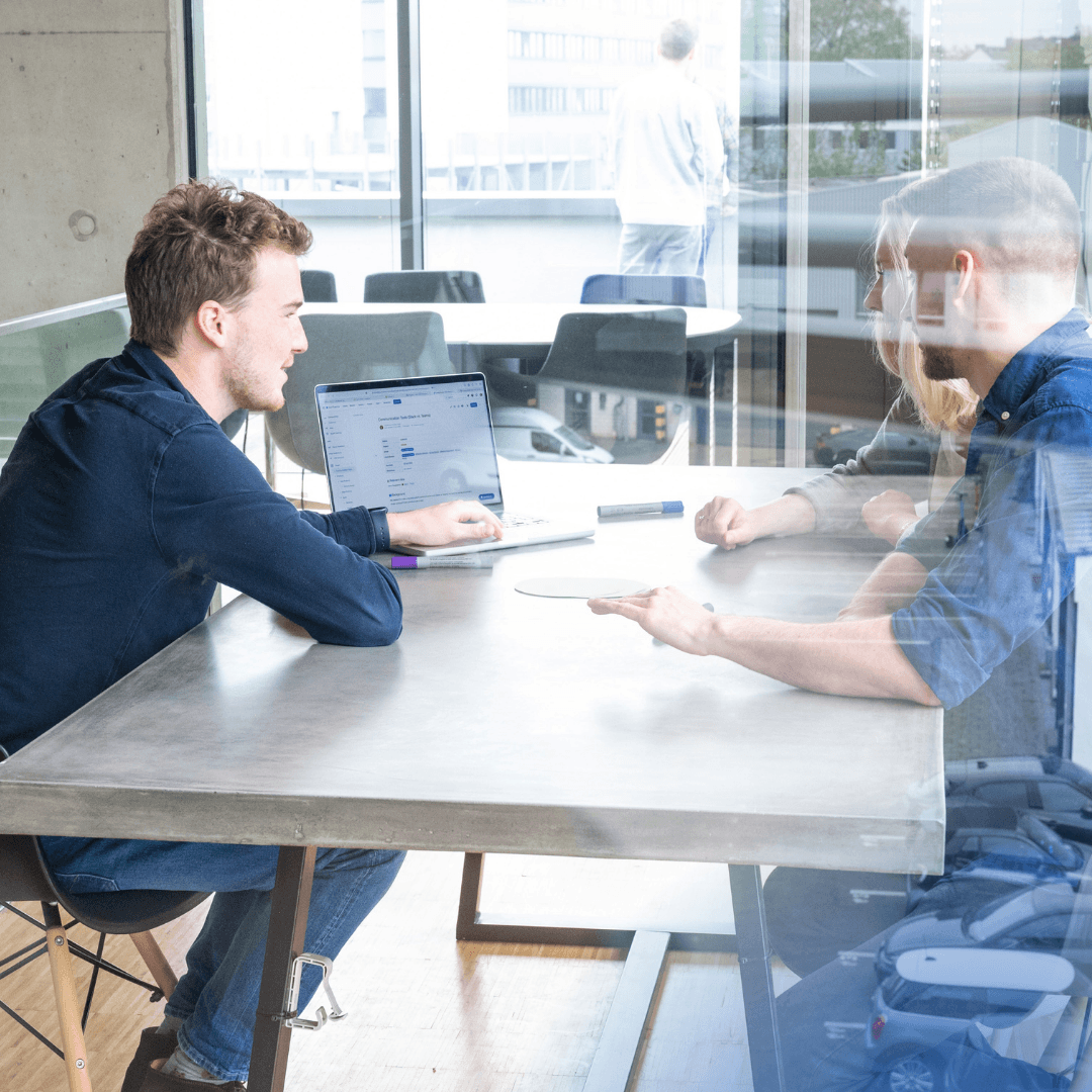 Zwei Männer diskutieren an einem Tisch mit Laptop.