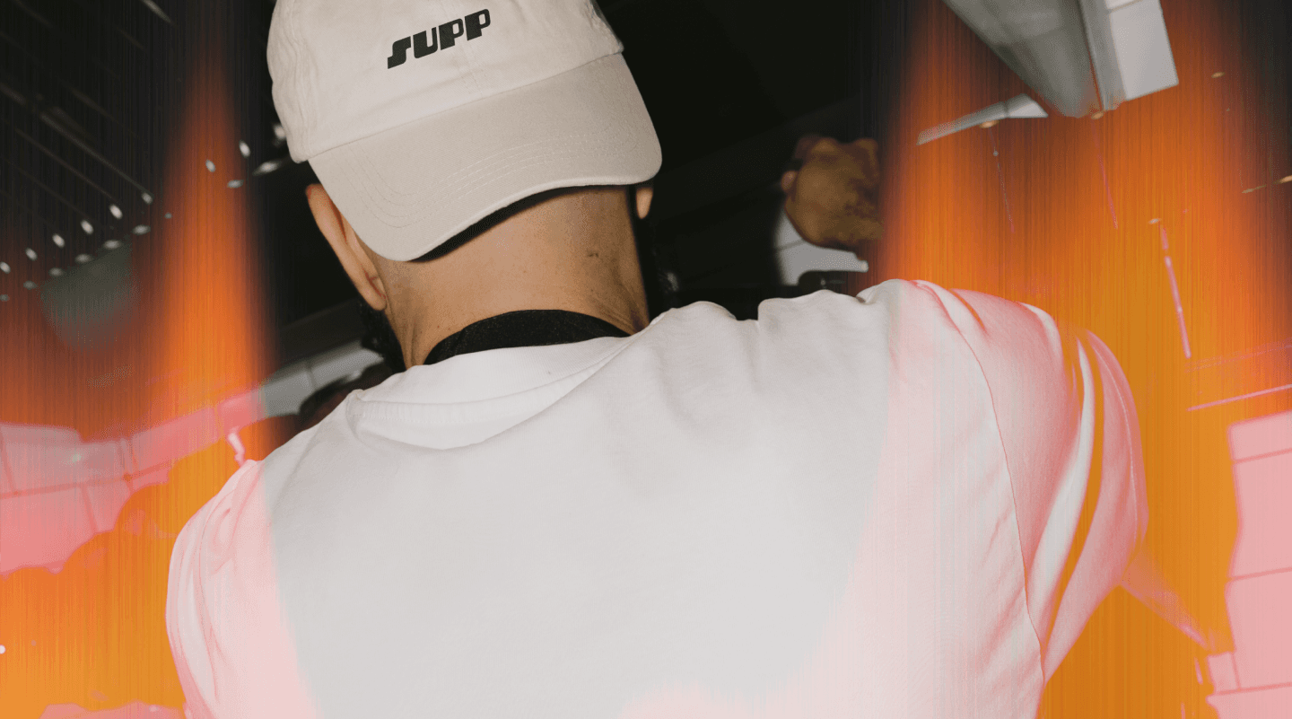 A person wearing a Supp branded cap, shot from behind in a busy venue