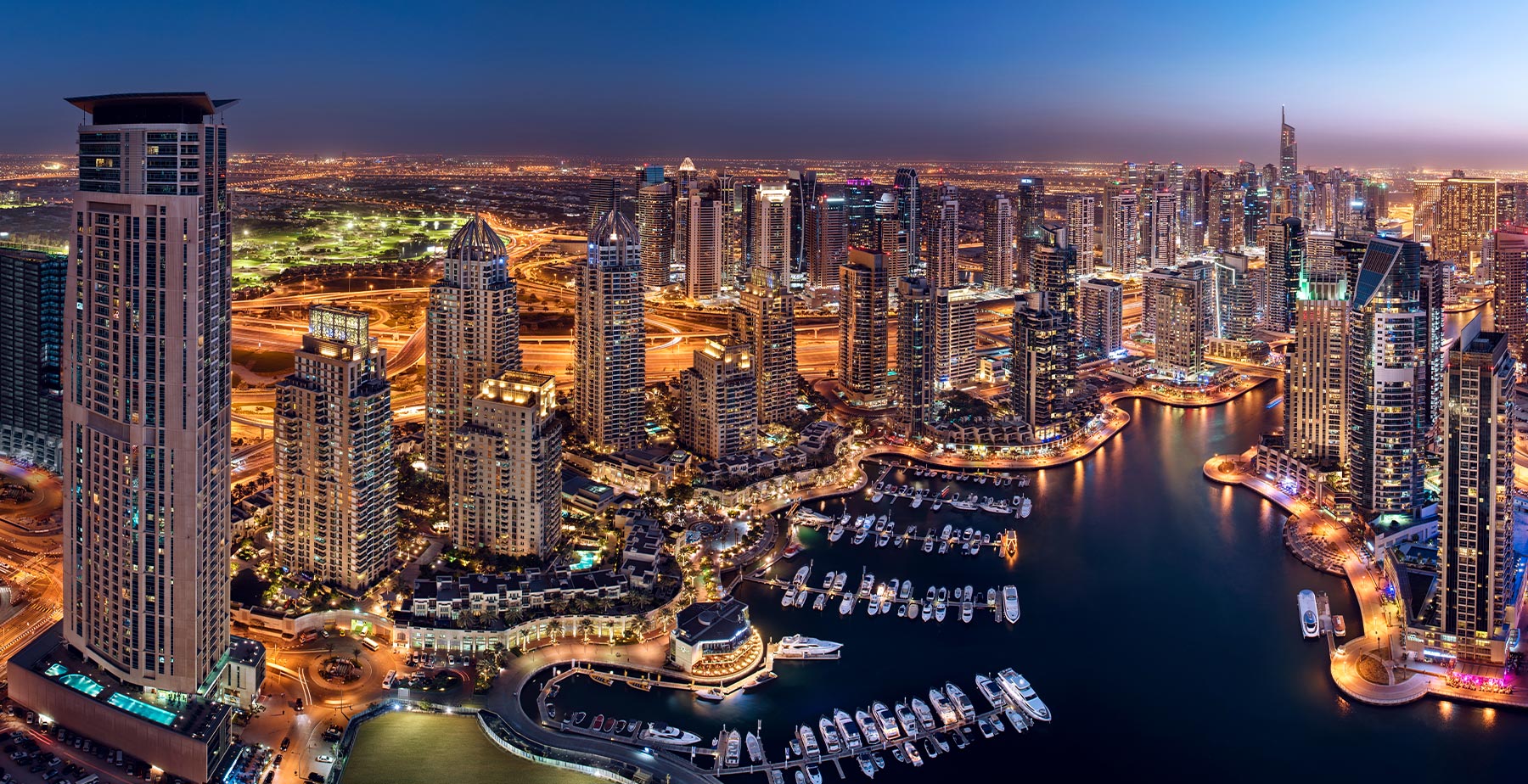 Abendliche Skyline von Dubai Marina mit beleuchteten Yachten und Wolkenkratzern.