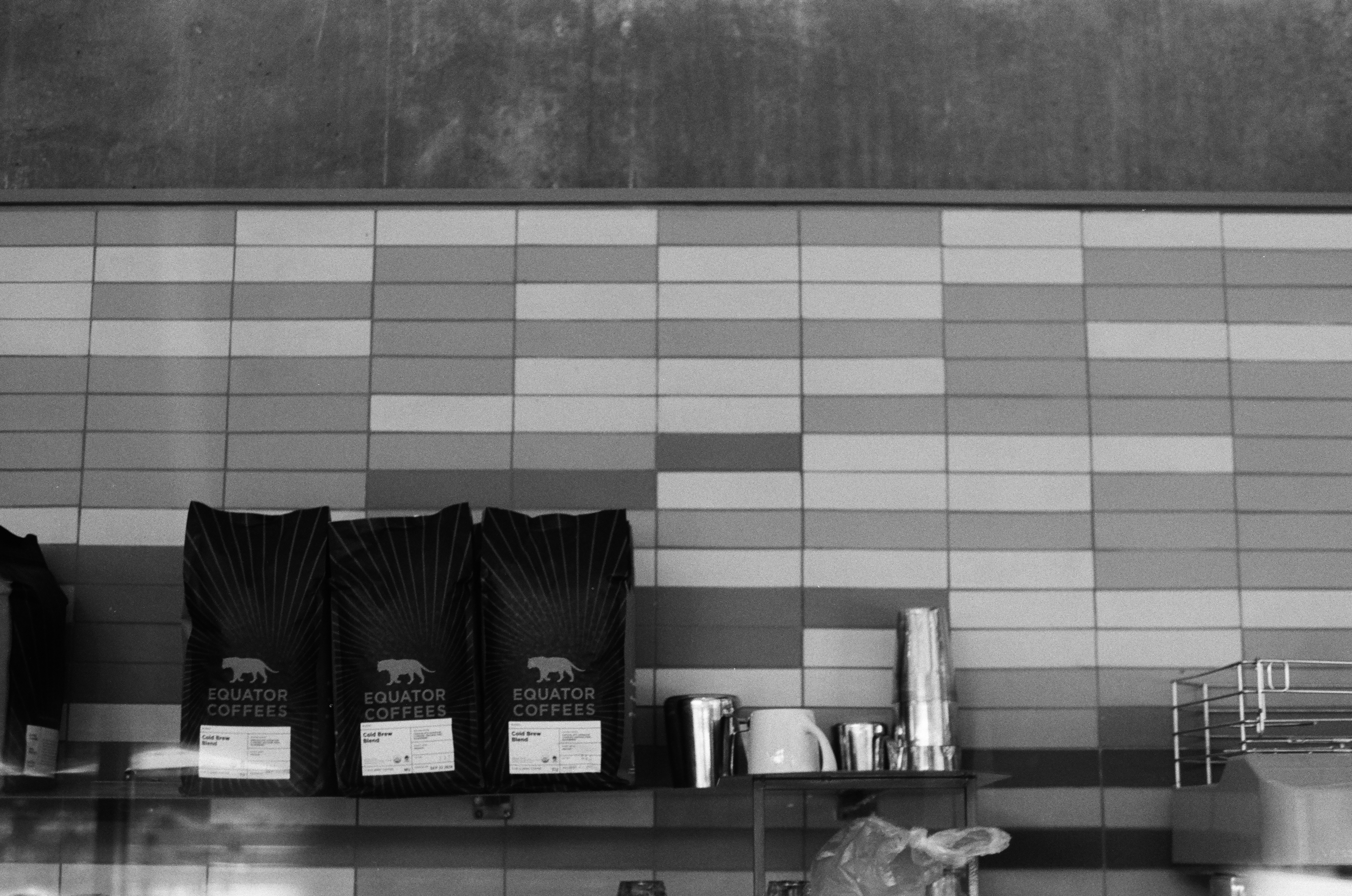 Equator Coffees bags and cups on a shelf against a patterned tile wall at the Culver City cafe.