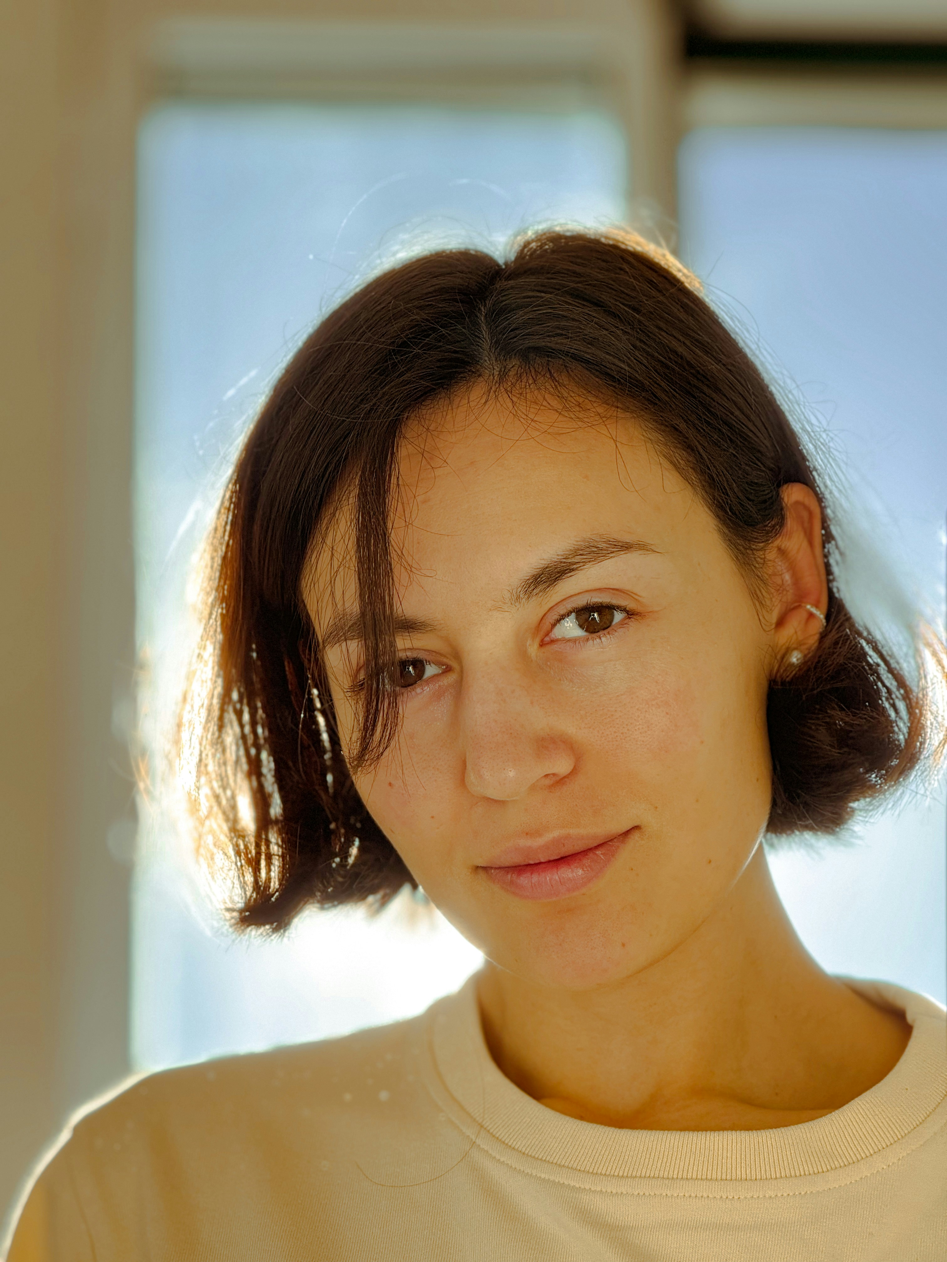 Young woman with short brown hair backlit by sun.
