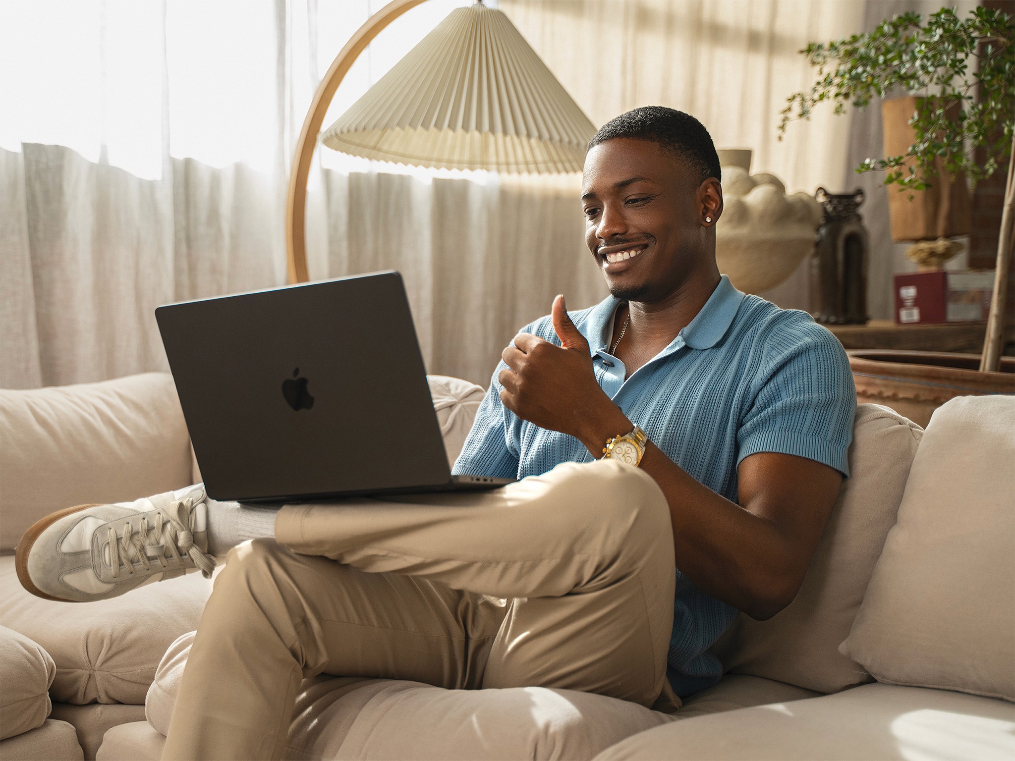 Young African American professional in late 20s watching UNBLOKD CO free coaching resources on laptop, seated on a beige sofa in a Japandi minimalist loft, dressed smart casual, smiling while learning Clarity, Alignment and inner leadership online.