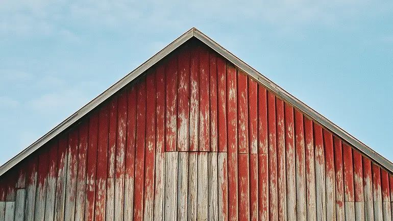 Top portion of a weathered red wooden barn under a partly cloudy sky