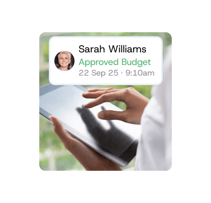 Hand holding a tablet displaying a notification “Sarah Williams – Approved Budget,” symbolising contractor verification and approval tracking.