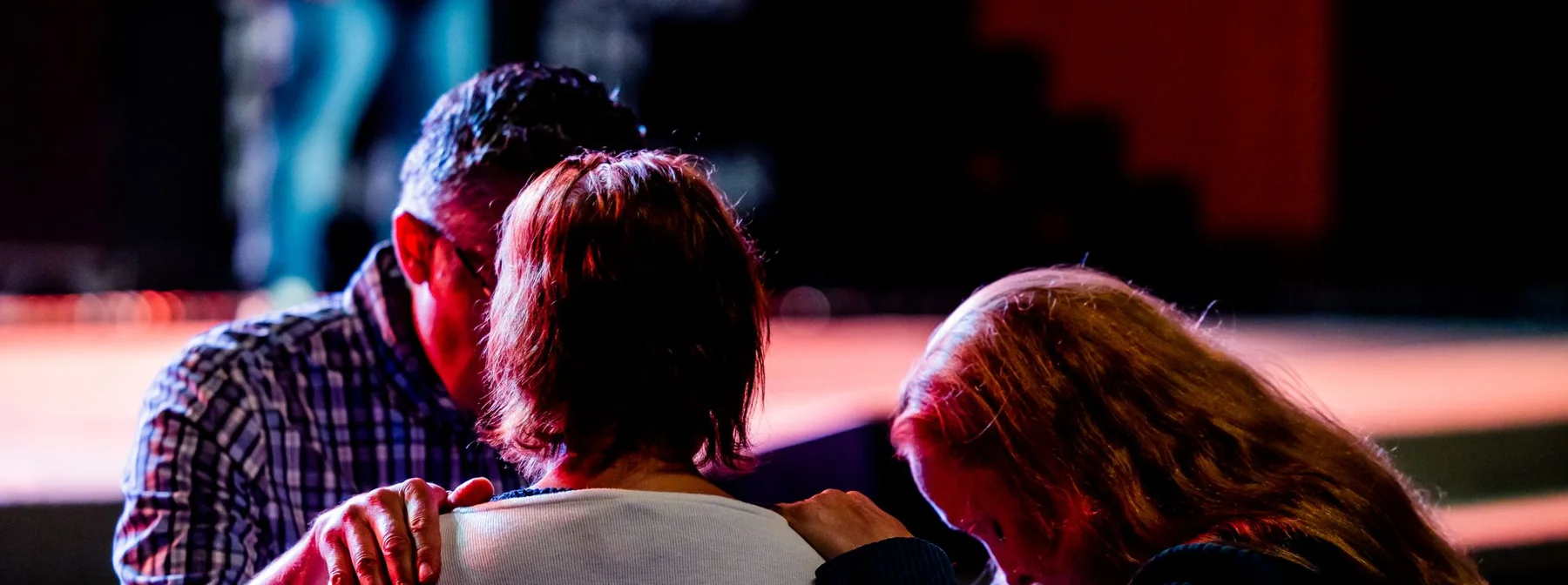 Three people praying together with hands on each other’s shoulders
