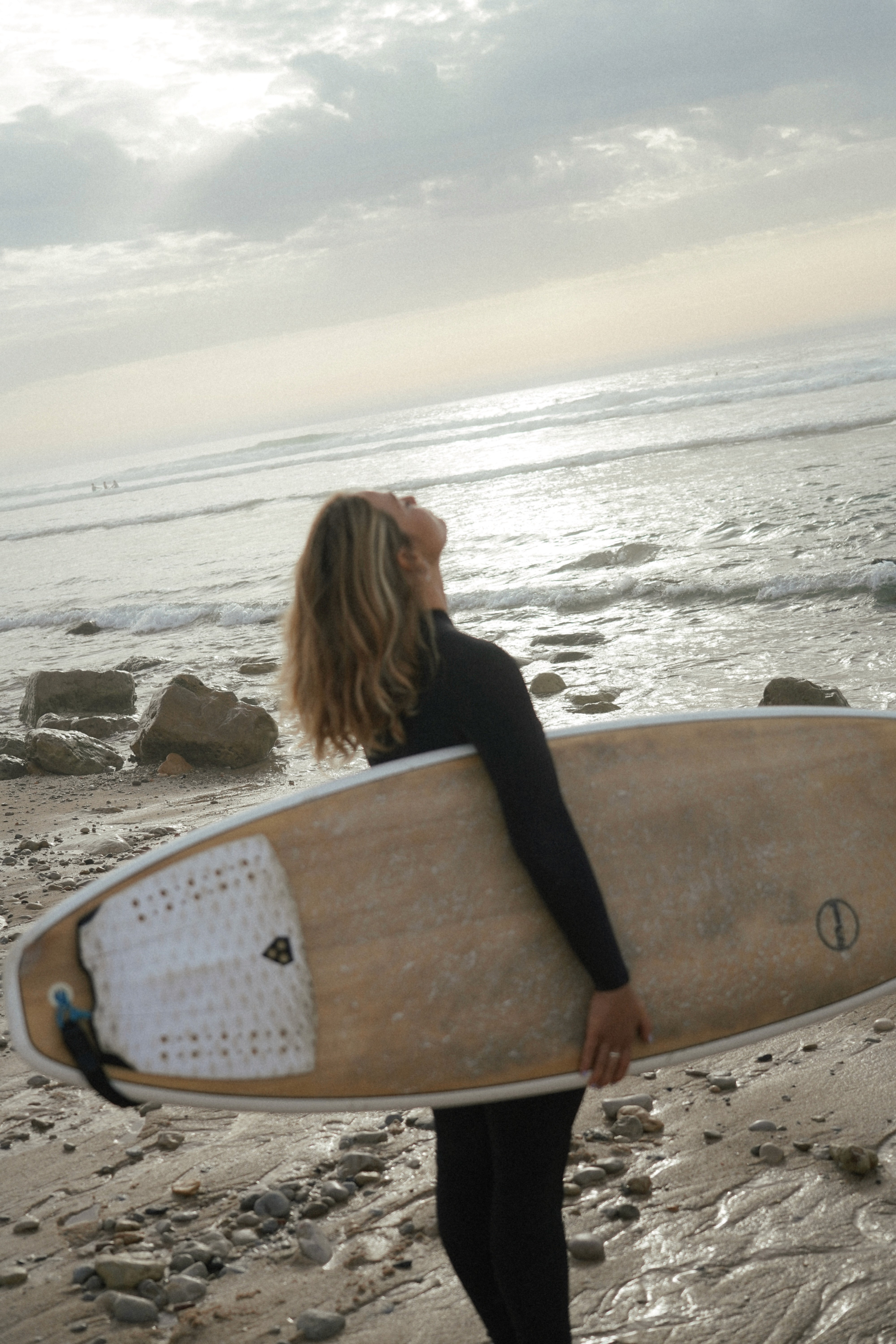 Mujer con tabla de surf en una playa rocosa
