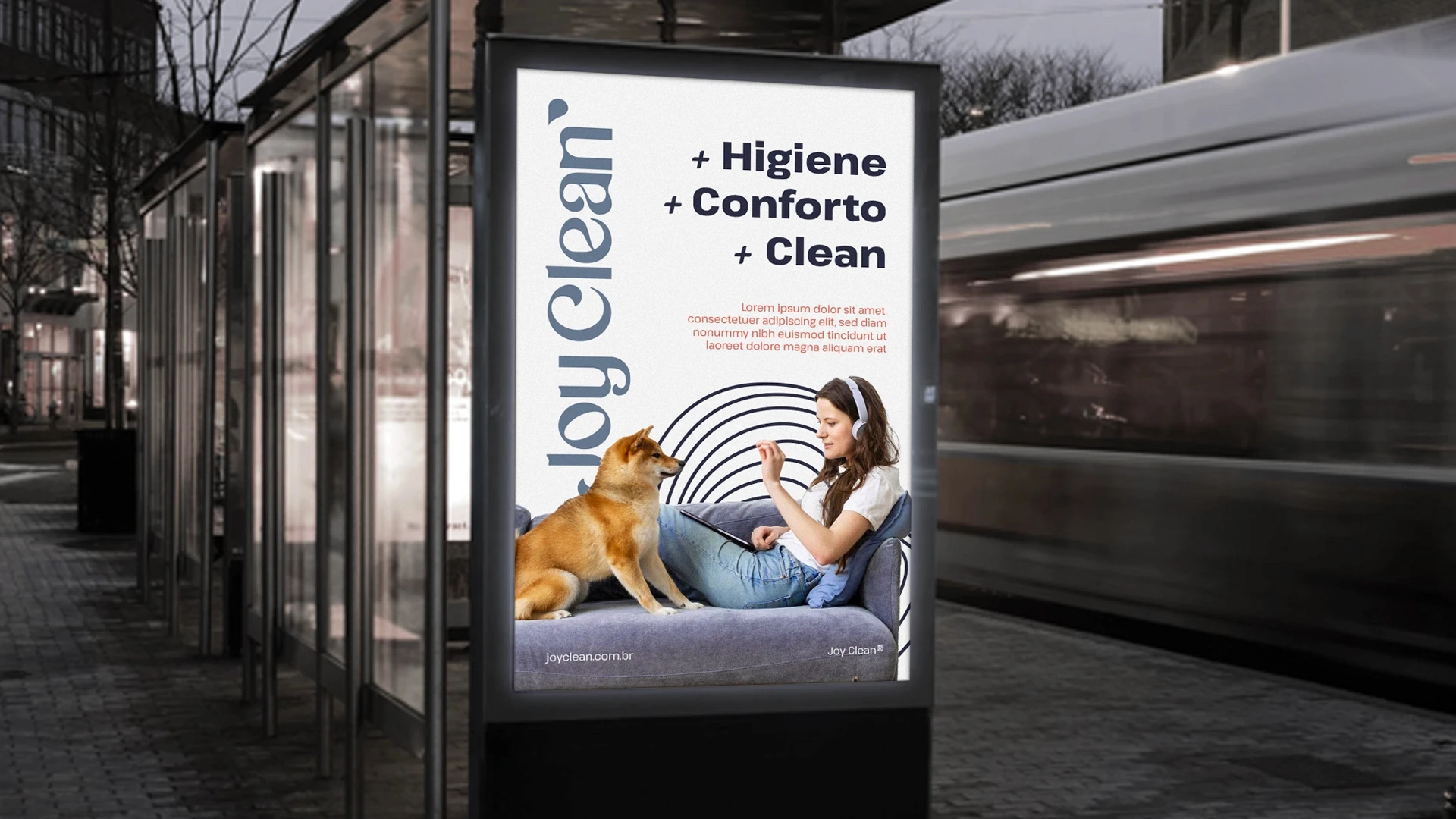 Display publicitário em um ponto de ônibus urbano à noite, exibindo cartaz da Joy Clean com o texto '+ Higiene + Conforto + Clean' e foto de mulher com seu cachorro no sofá.