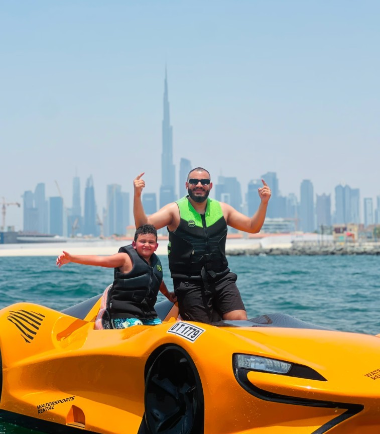 Man and son pose on a water car with the view of the Dubai skyline in the background.