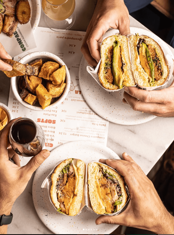 Personnes dégustant des burgers gourmets à l’avocat avec des pommes de terre croustillantes et un verre de vin rouge au restaurant latino Compadre, près de Notre-Dame à Paris