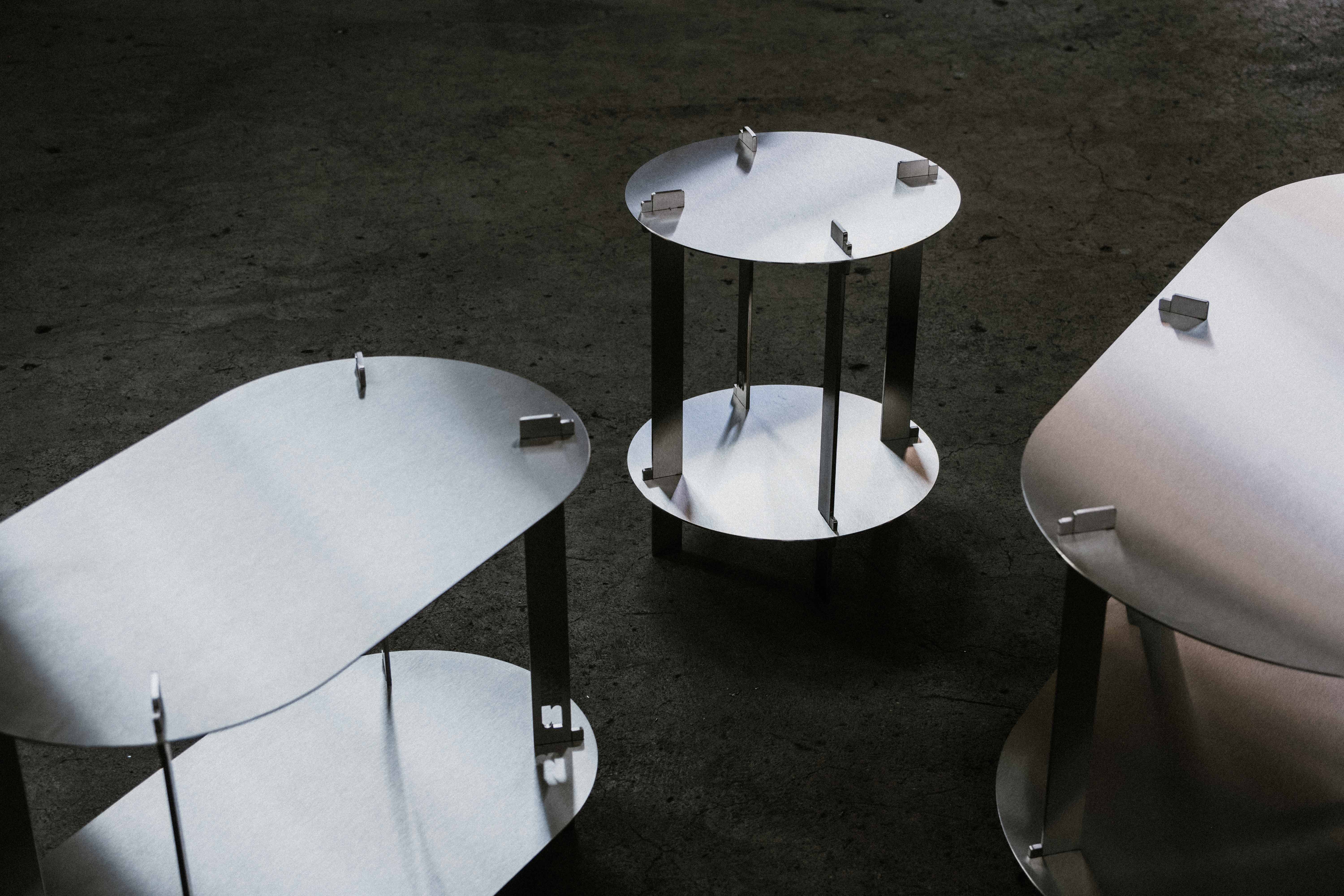 Closeup of Three steel Coffee Tables in a workshop, sun shining on the scene
