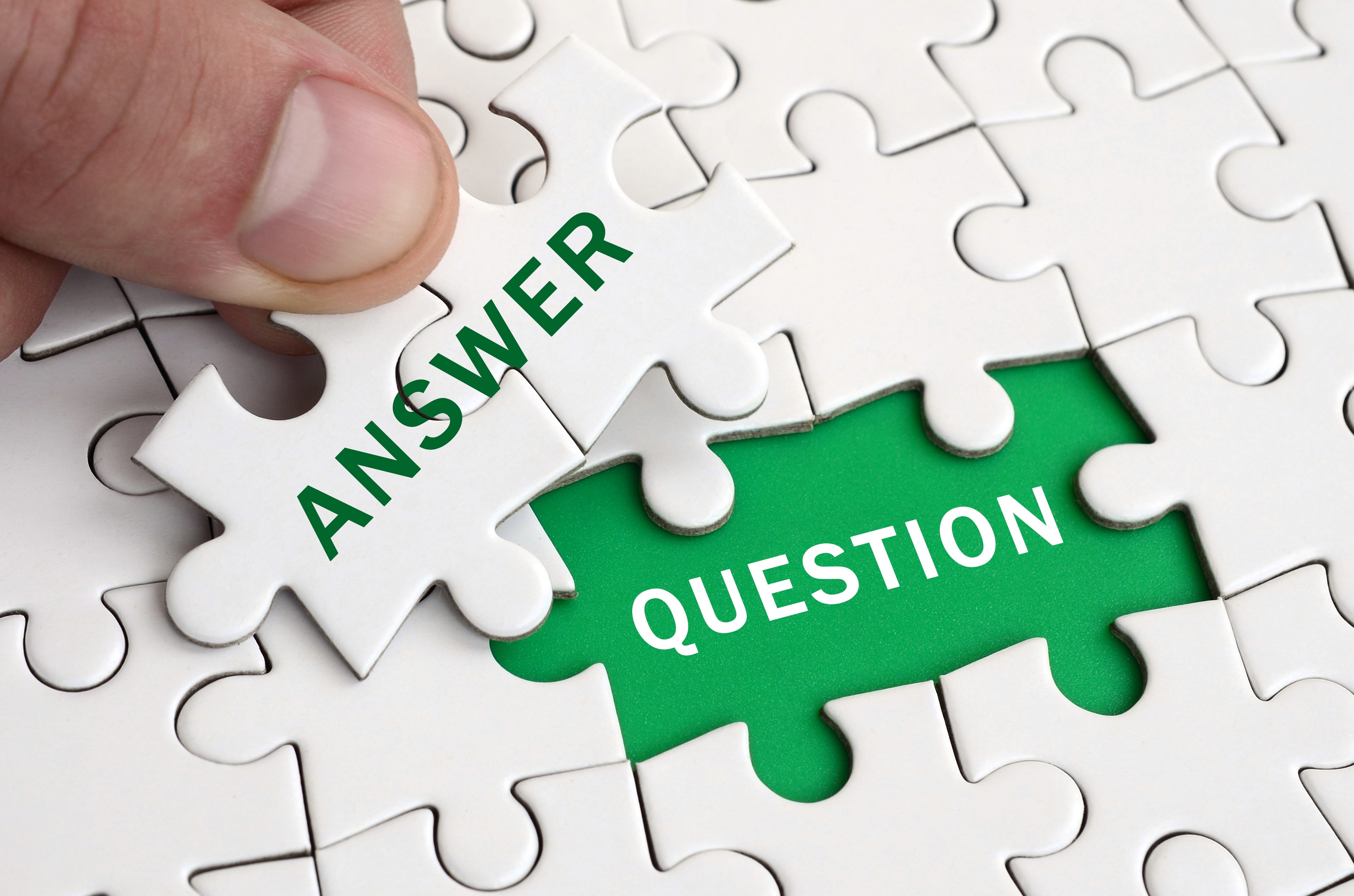 A hand placing a puzzle piece labeled Answer into a gap revealing the word Question on a green background, representing the core concept of Answer Engine Optimization and how AI systems match questions to authoritative answers