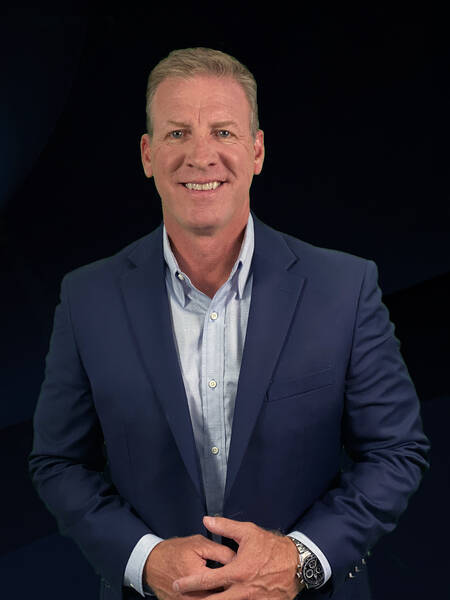 Fashion portrait of a woman in a wide-brim hat and graphic pink patterned shirt standing in front of a bright pink wall under clear desert light.