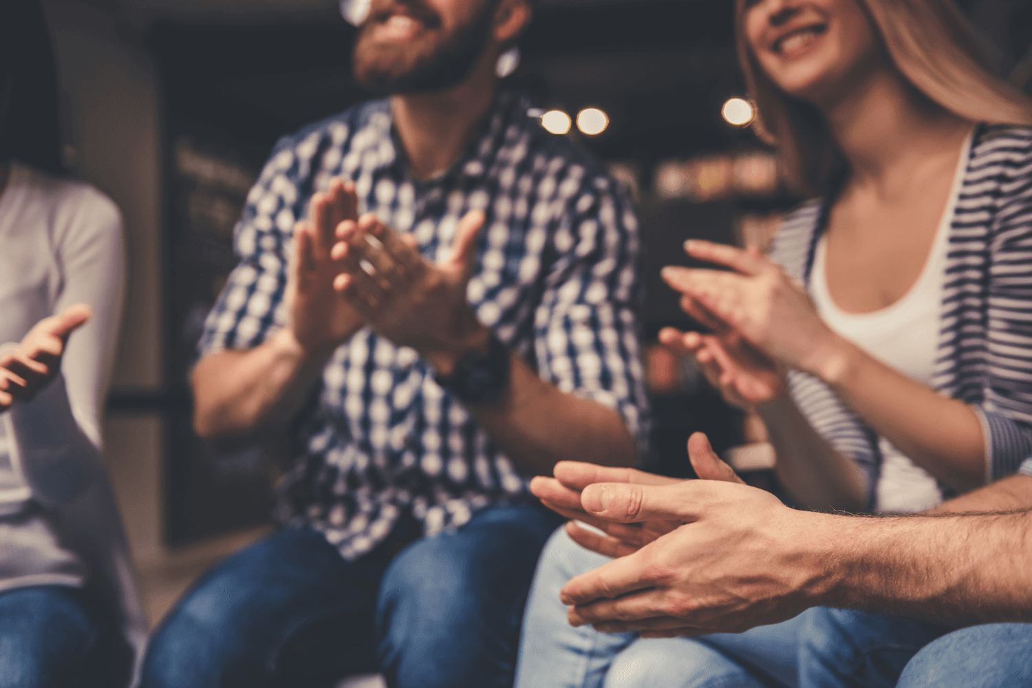 A circle of people sitting cross-legged, meditating with hands in a prayer position. Soft, warm lighting.
