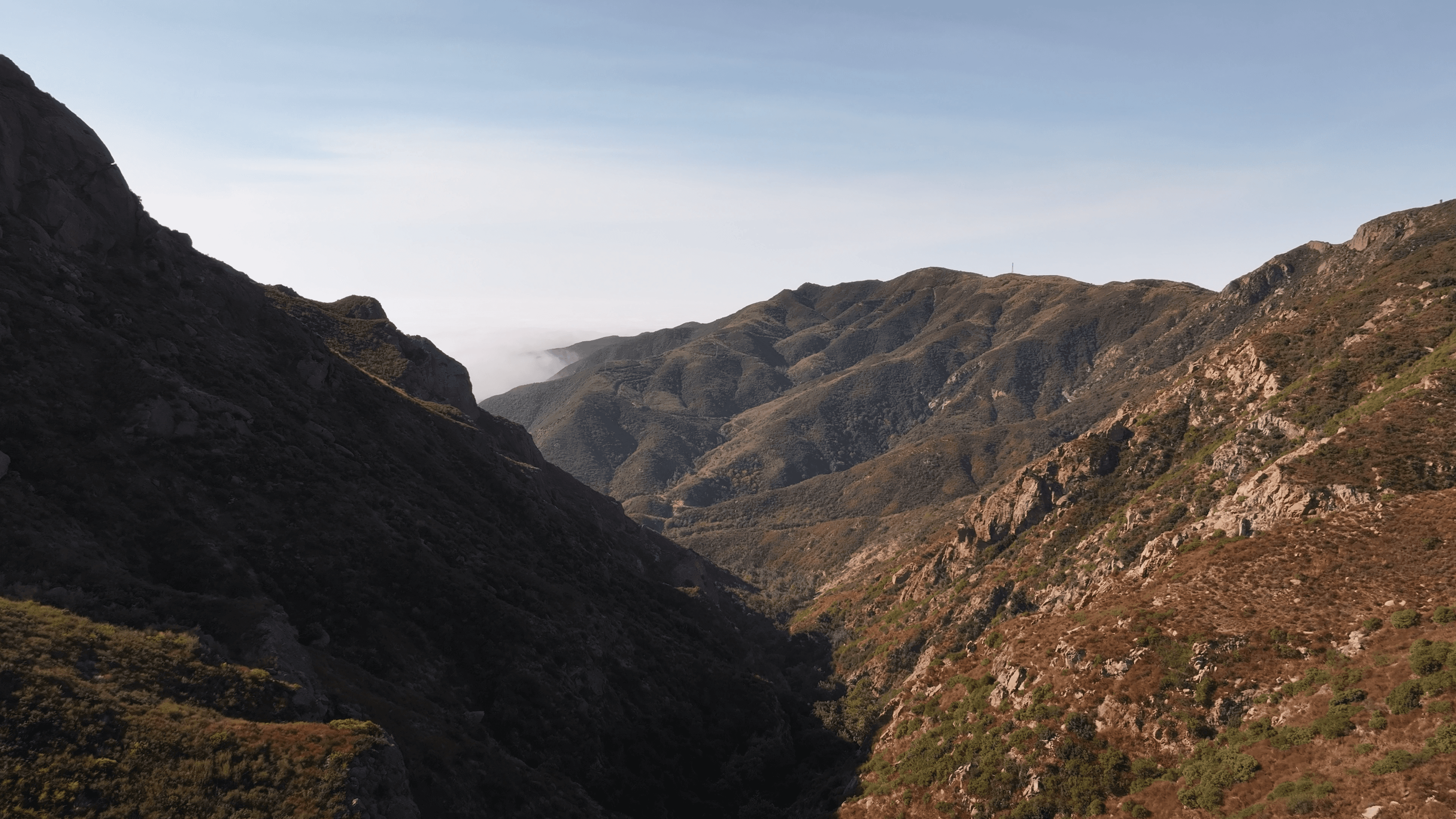 a sweeping view of the Santa Monica Mountains near Malibu — rugged brown and green hillsides frame a canyon where marine layer fog drifts through.