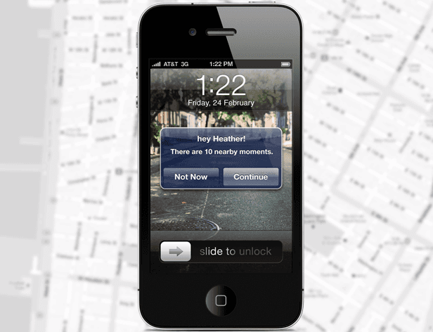 A black iPhone displays the lock screen on Friday, February 24th at 1:22 PM. The screen shows a blue notification box with the message "hey Heather! There are 10 nearby moments." Below the message are two buttons: "Not Now" and "Continue". The phone's home button is visible at the bottom. The background behind the phone is a blurred map.