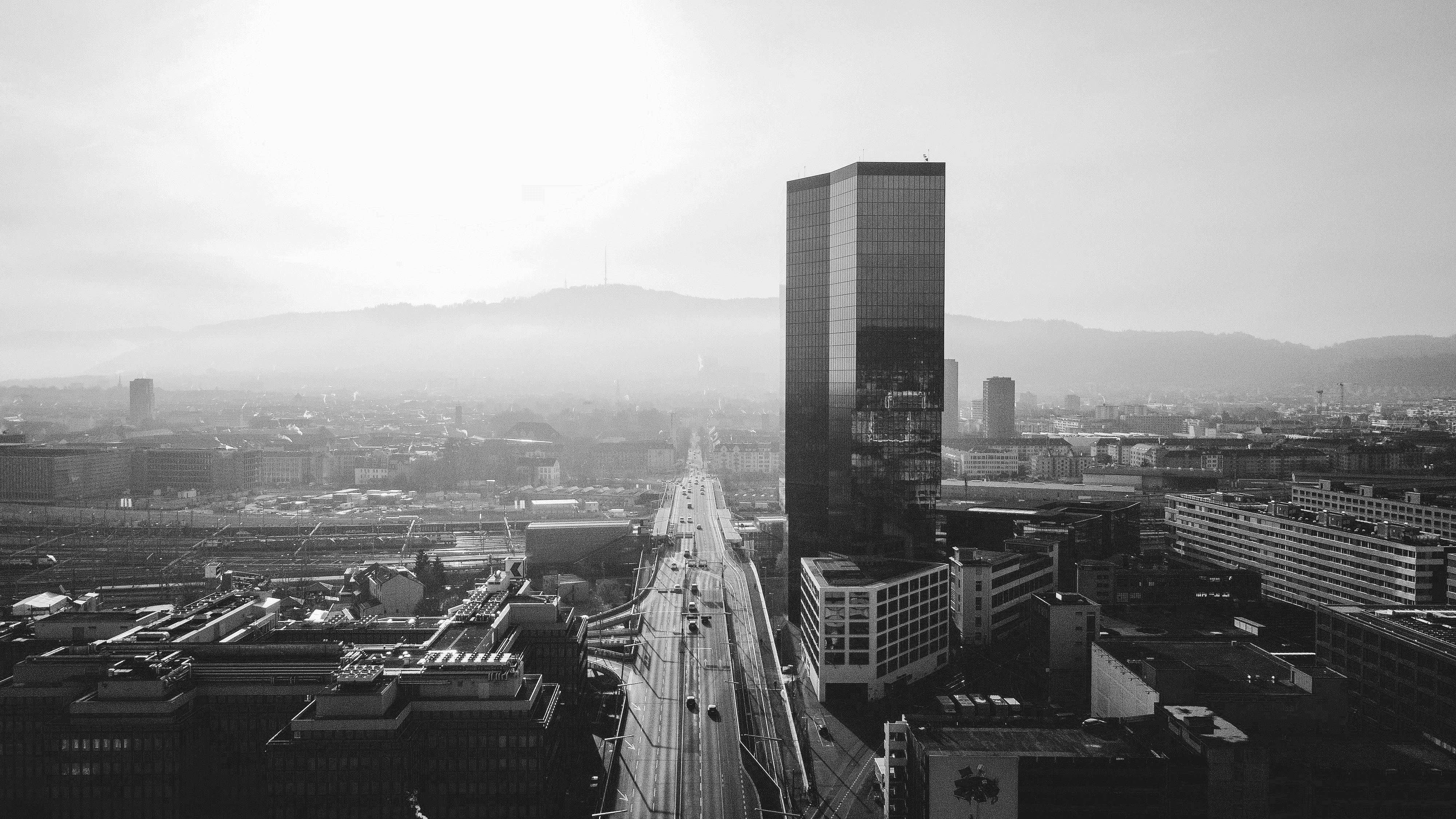 Black-and-white skyline of Zurich with a tall modern office tower and a highway leading into the city.