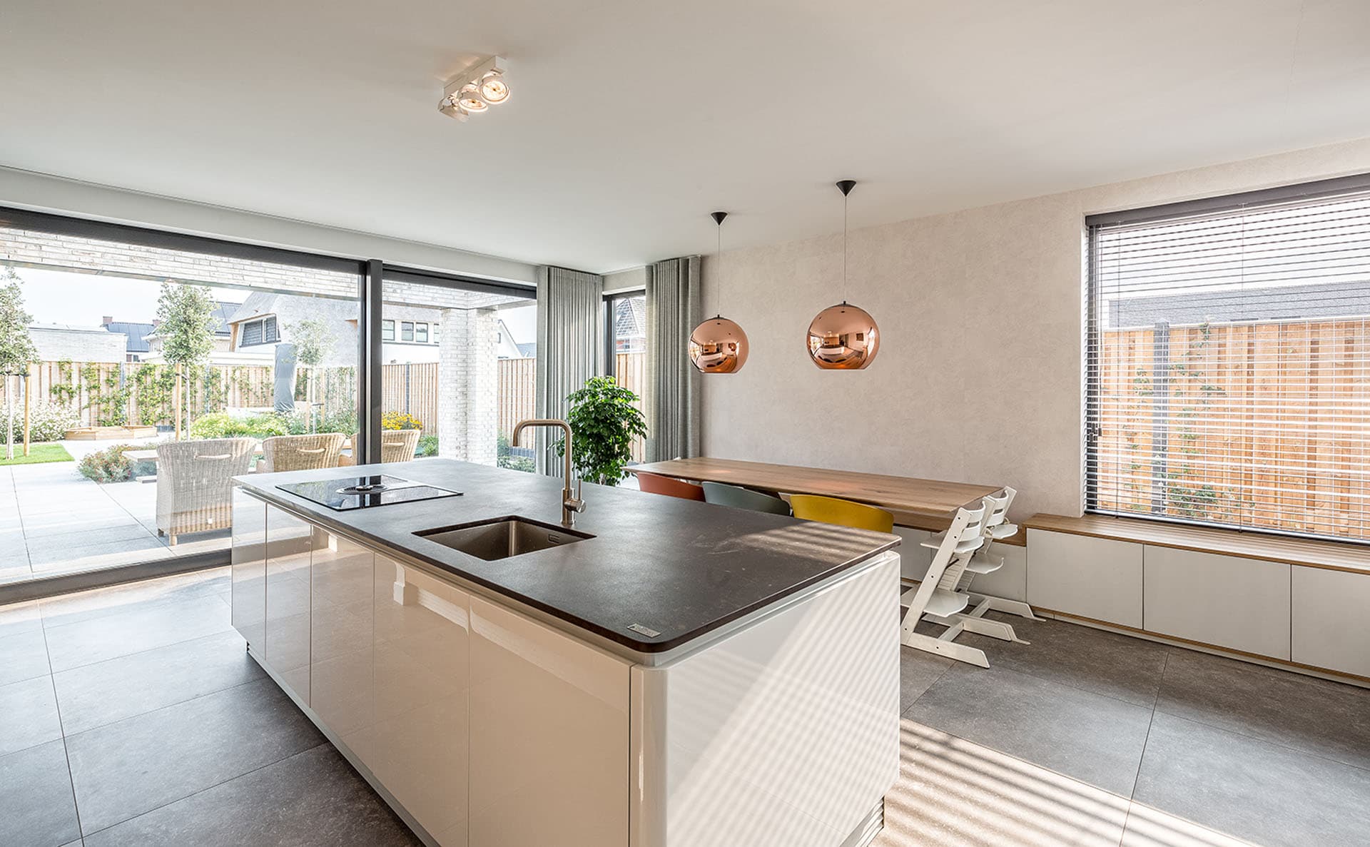 Moderne keuken met houten kastenwand, wit kookeiland en grote koperkleurige hanglamp