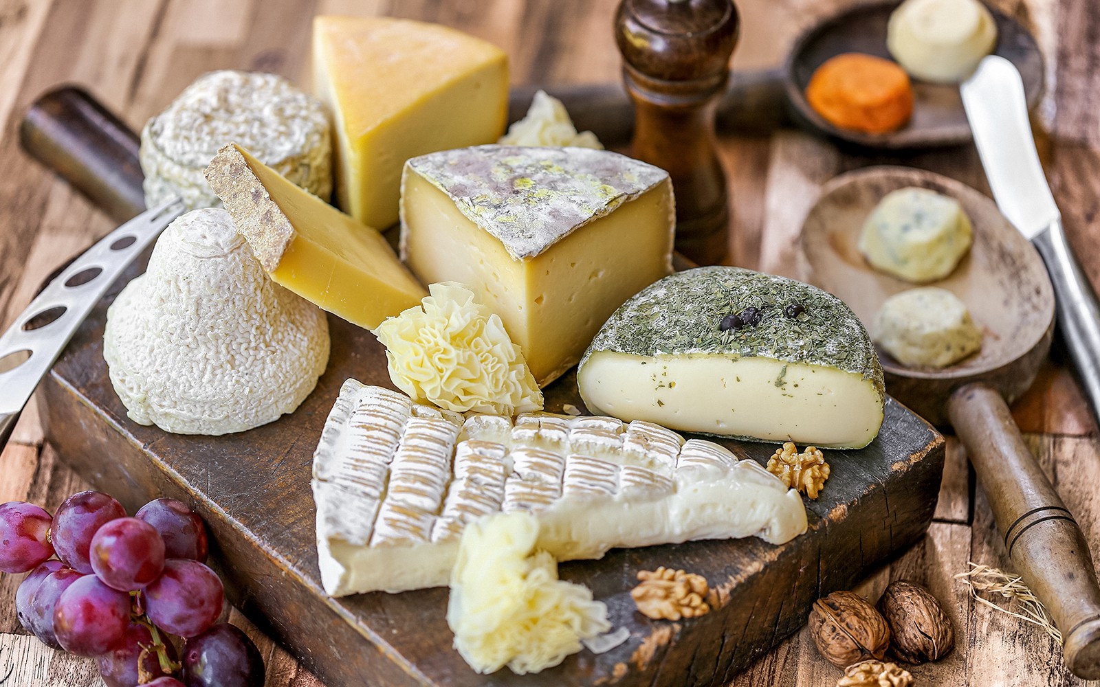 Queijos franceses variados e uvas em uma tábua de madeira, destaque nos passeios gastronômicos de Paris Saint Germain.