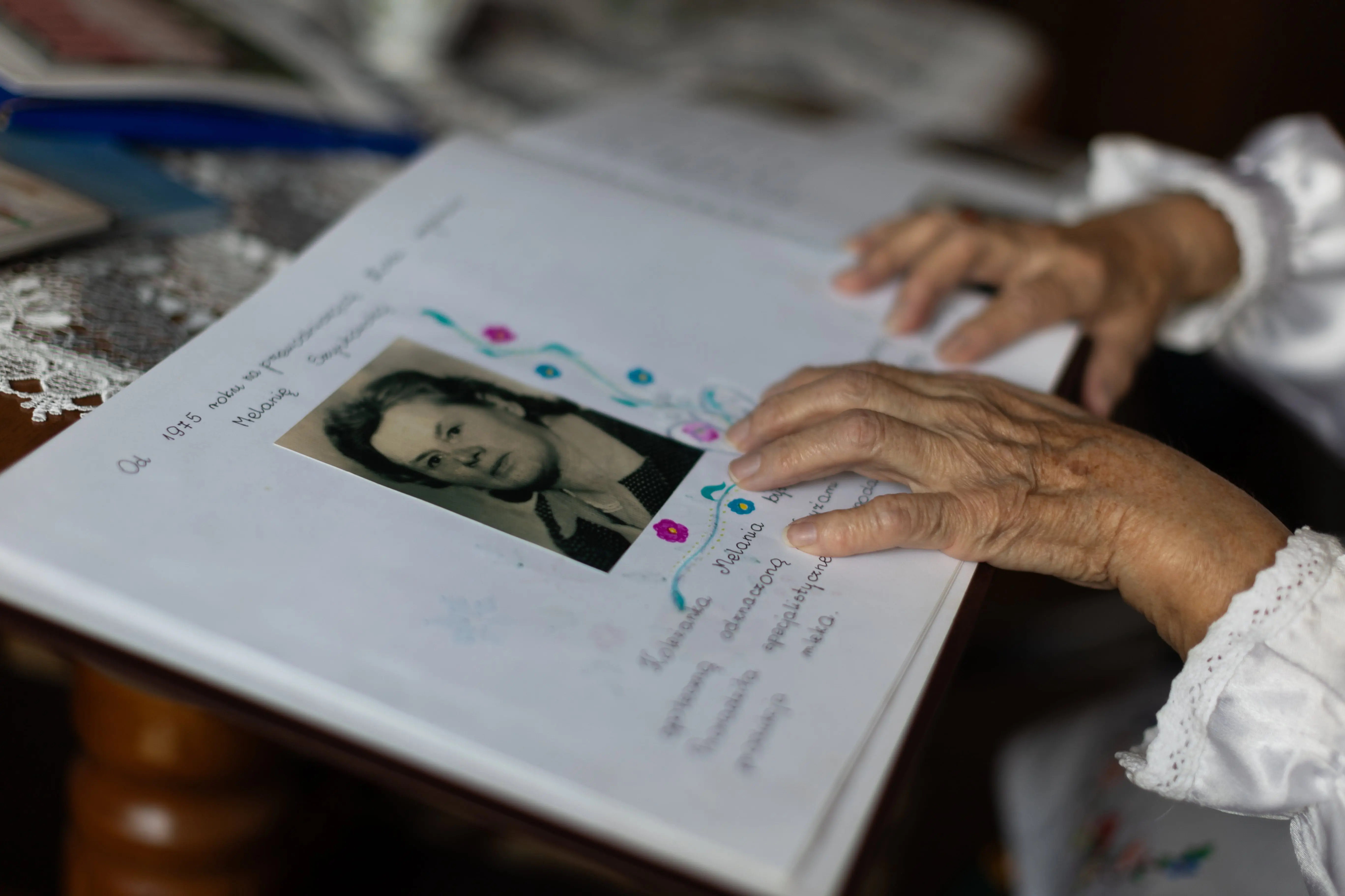 Ręce starszej osoby położone na albumie. Na kartce albumu jest stara fotografia oraz podpis.
