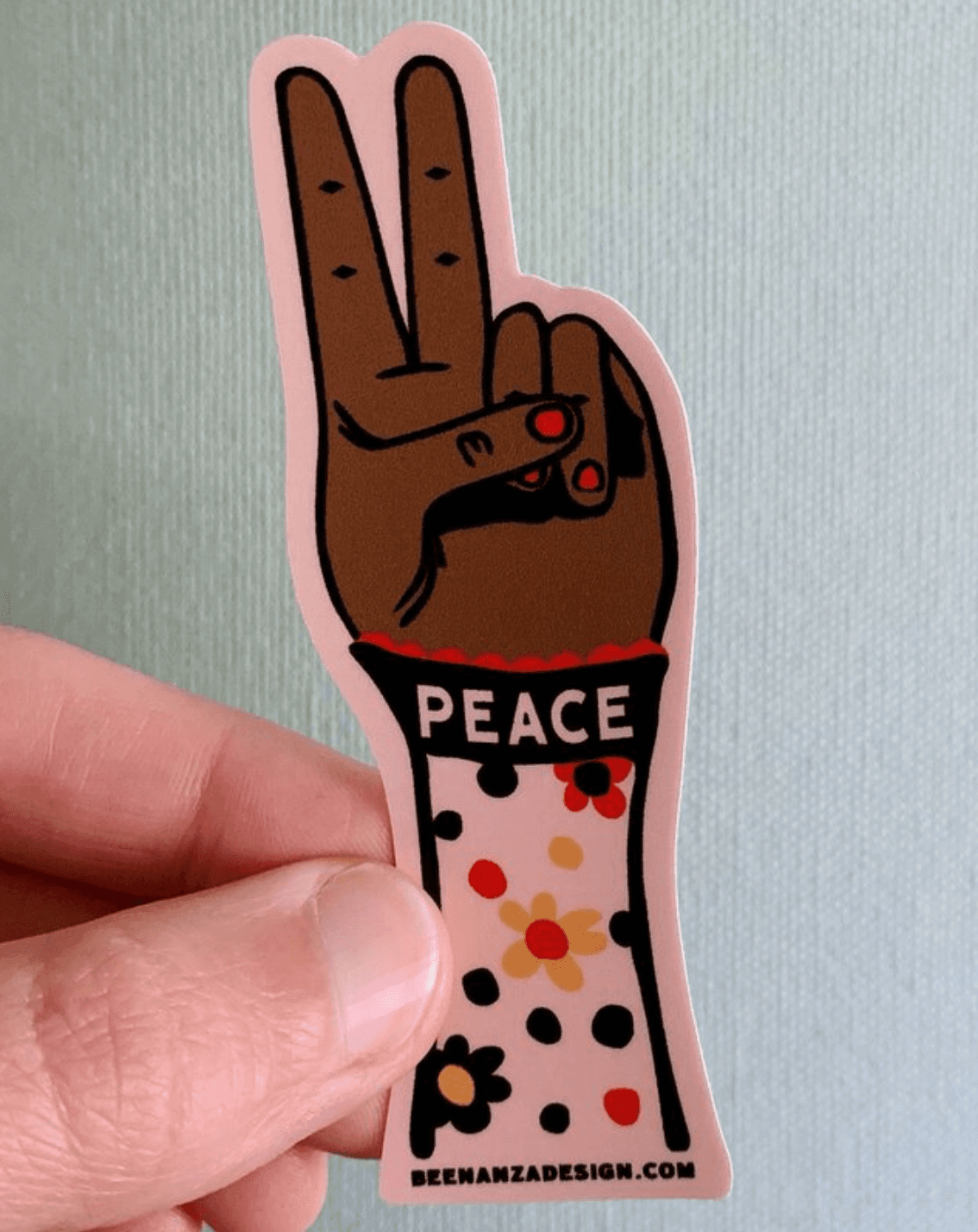 person holding a sticker of a hand giving a peace sign that says "peace"