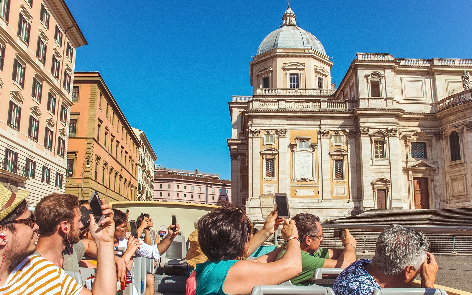 Tourists on a hop-on hop-off bus tour in Rome, photographing a historic building.