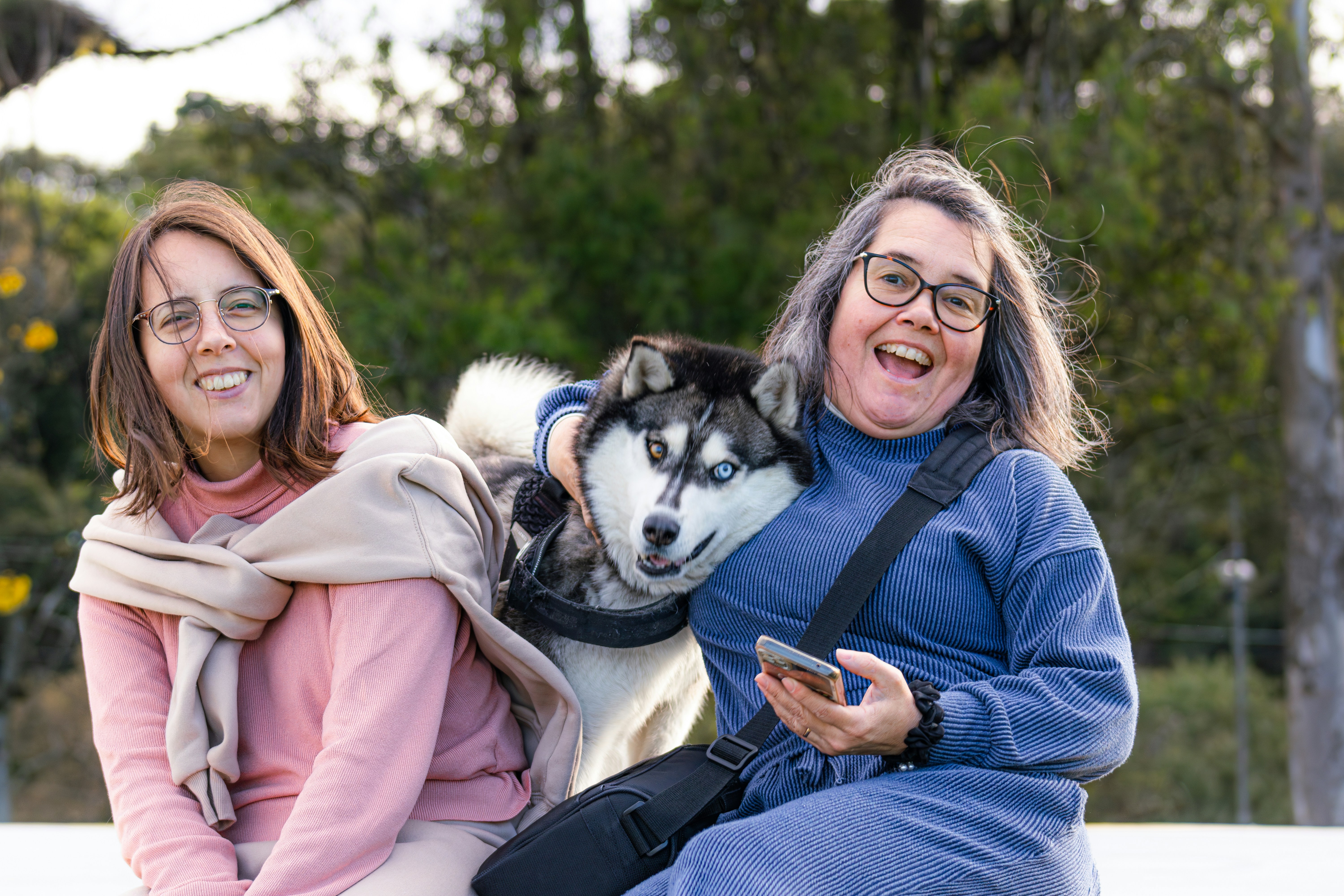 Two women and a husky dog smiling outdoors