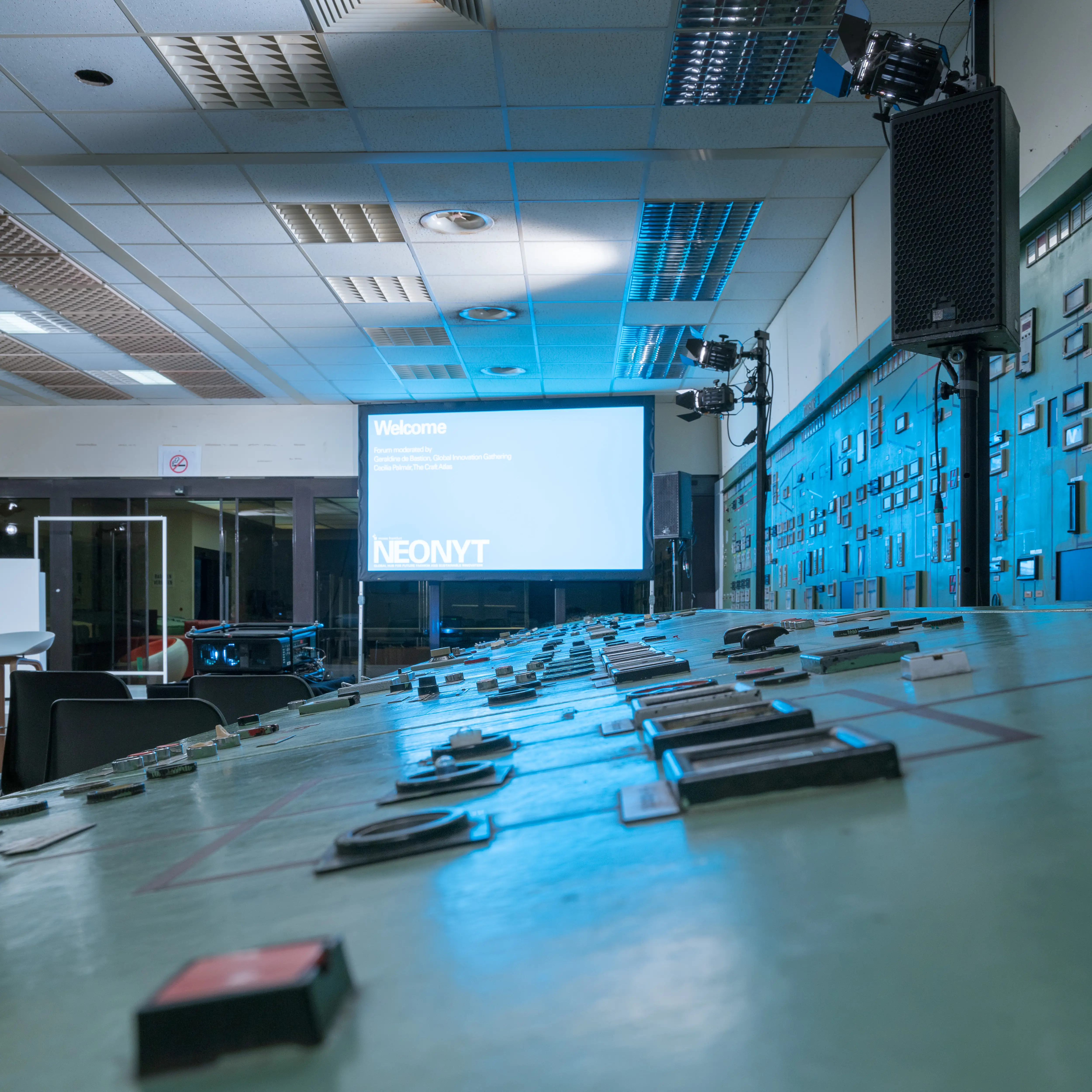 Vintage control desk with switches in front of the NEONYT welcome screen in the blue-lit control room at Kraftwerk Berlin.