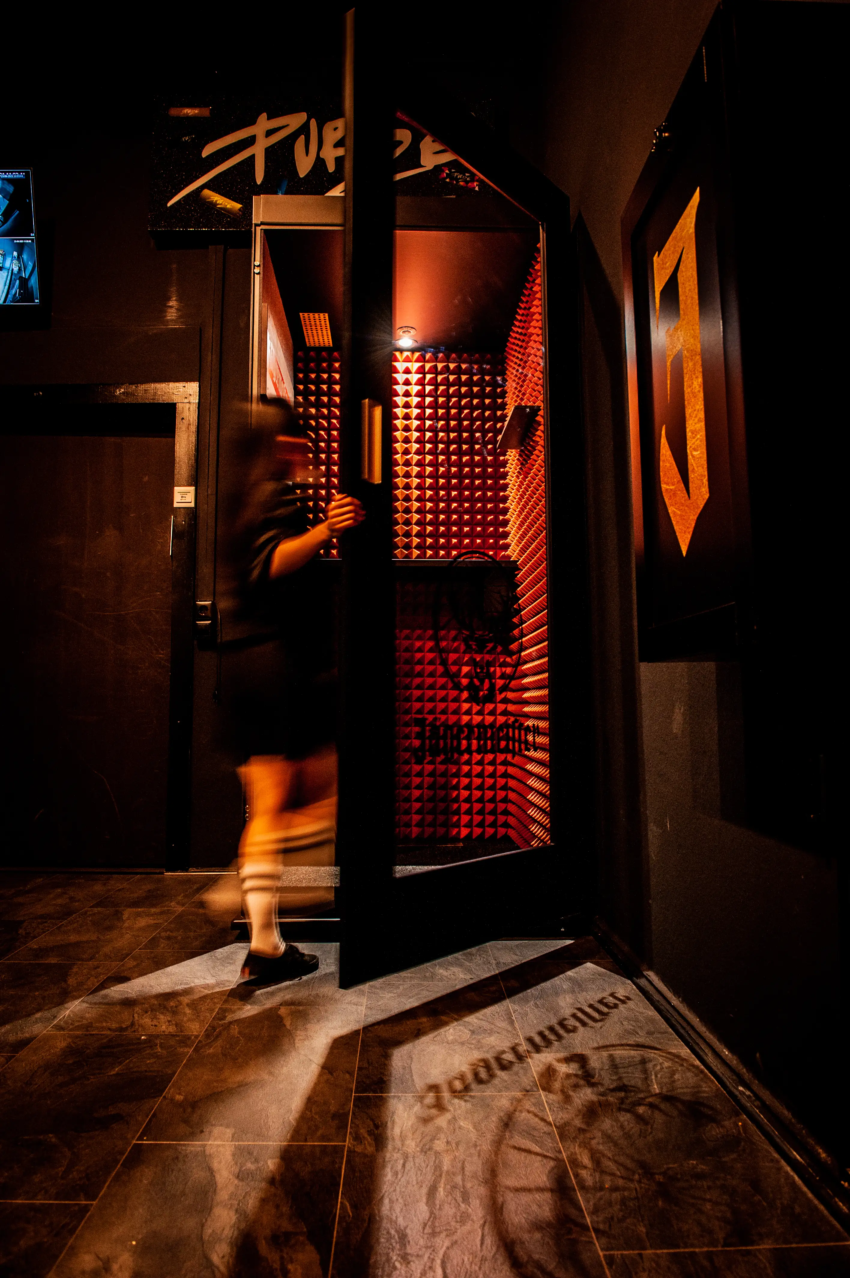 Entrance to the JÄGERMEISTER x SVENNI'S space with a person walking through a door into a corridor lined with orange-lit acoustic foam pyramids and a Jägermeister floor logo.