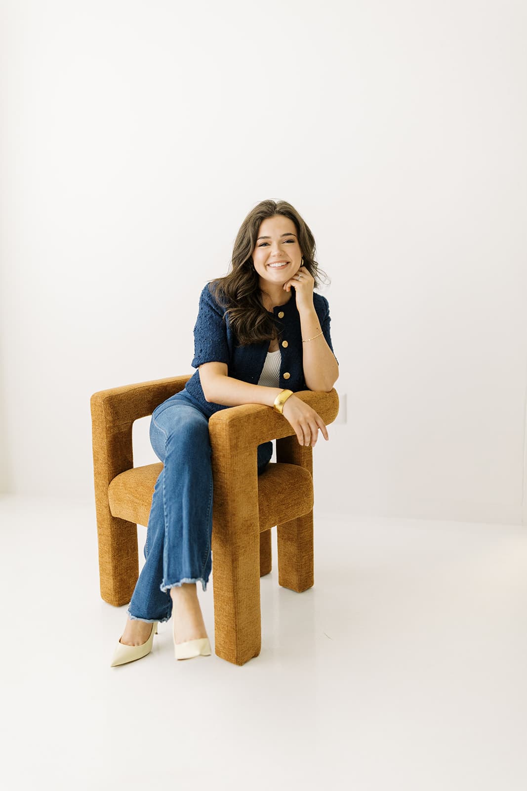 A model smiles while seated in a stylish chair at Revelator Studio in Shreveport, photographed by Andy Roberts, showcasing the studio’s natural light and modern design ideal for creative sessions.